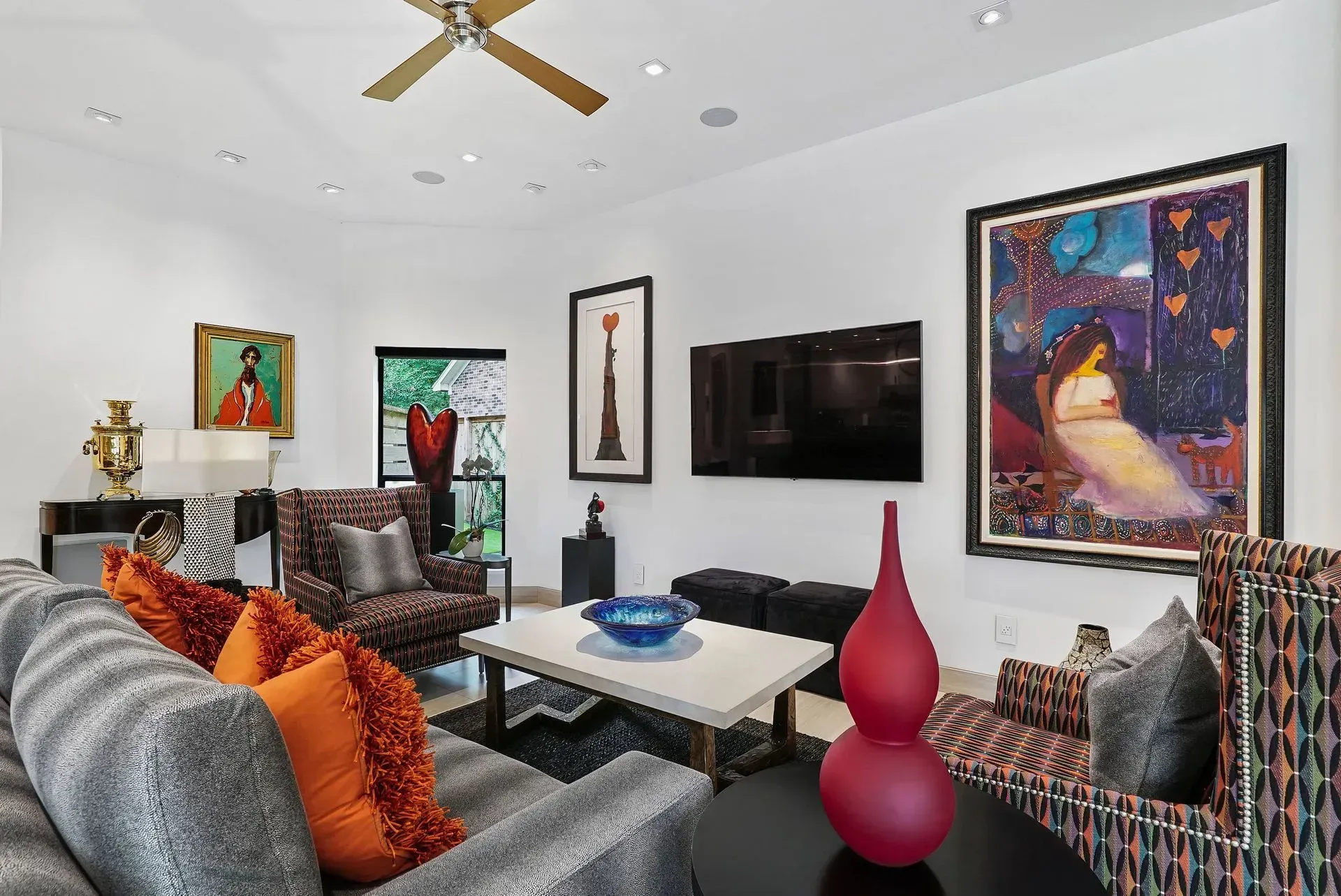 Modern living room with patterned sofas, wall art, a TV, and a red vase centerpiece.