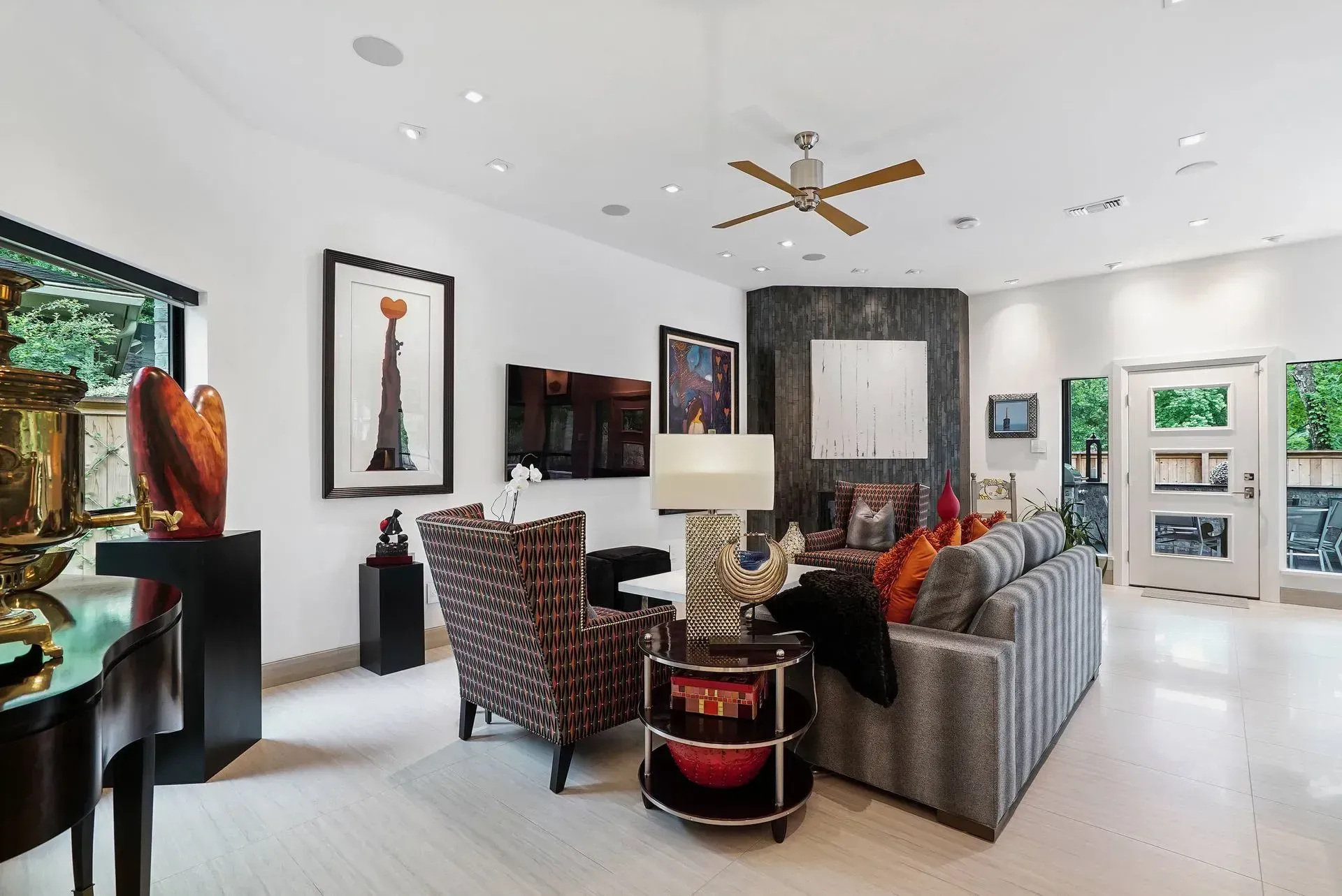 Modern living room with patterned seating, abstract art, ceiling fan, and bright windows