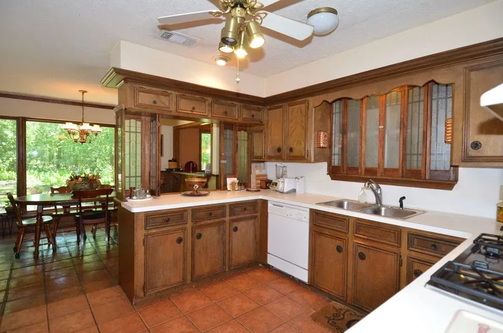 Bright kitchen with wood cabinets, white counters, terracotta tile, and sliding doors to a dining area.