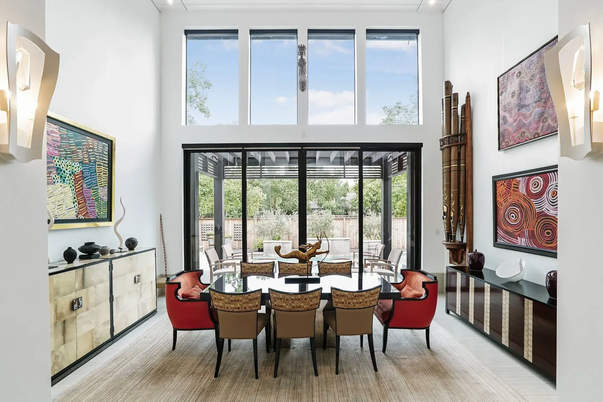 Bright modern dining room with a long table, red chairs, large windows, and garden view