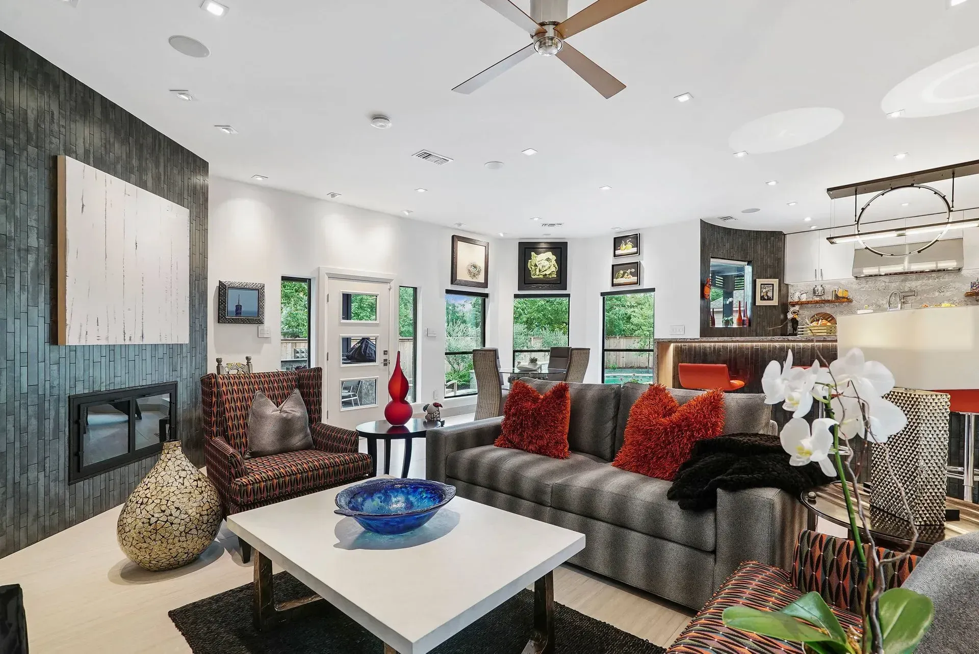 Modern living room with gray sofa, white coffee table, red pillows, wall art, and ceiling fan