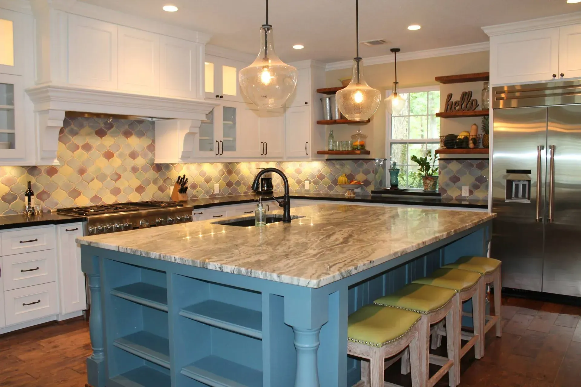 Bright kitchen with blue island, marble countertop, white cabinets, colorful backsplash, and stools.
