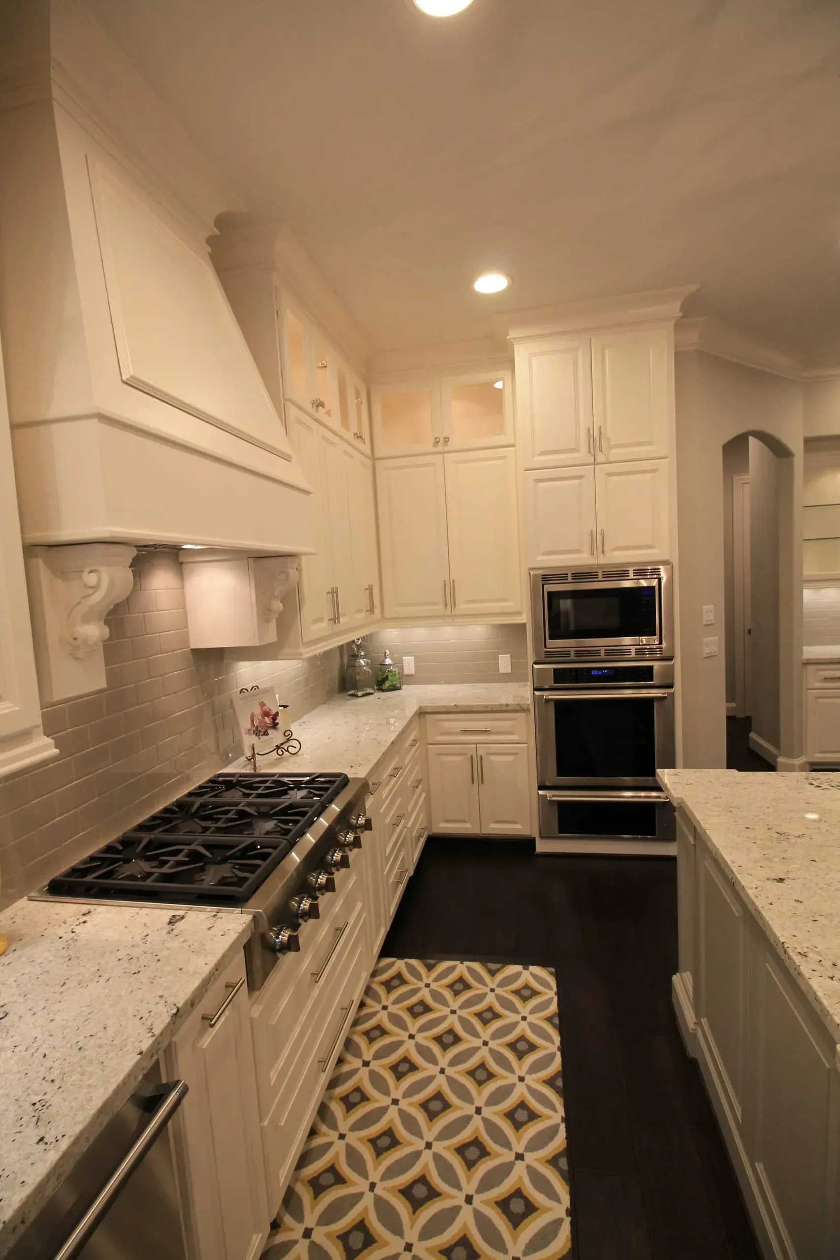 Bright white galley kitchen with granite counters, patterned runner, built-in oven, and gas range.