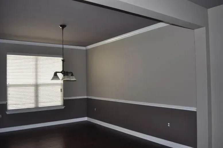 Empty dining room with gray walls, dark floor, white trim, and a hanging light by a window