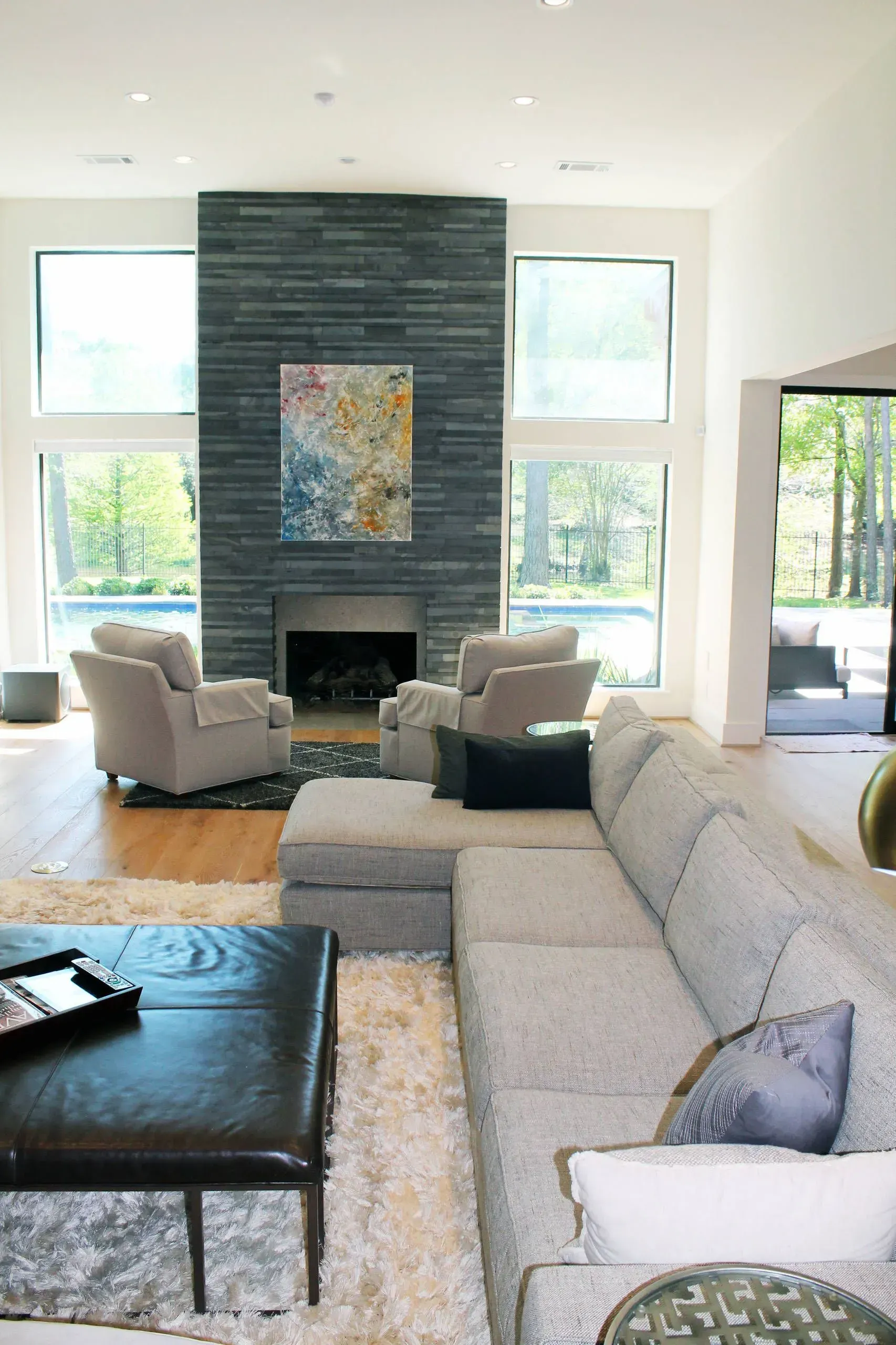 Modern living room with gray sectional, black ottoman, fireplace, and large windows.