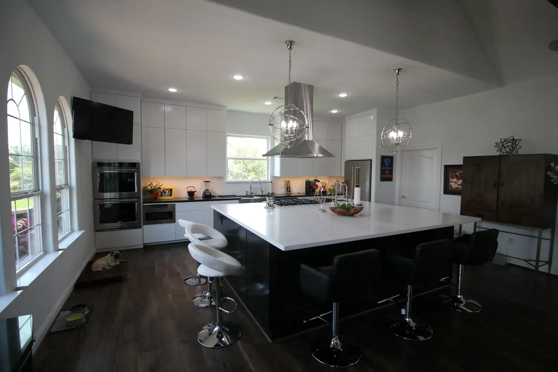 Modern kitchen with large white island, black stools, stainless range hood, and dark wood floors