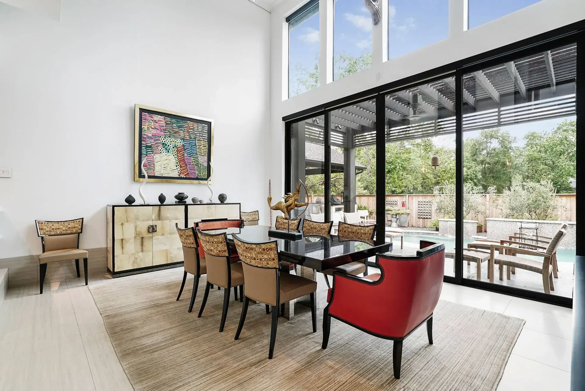 Bright dining room with a long table, red chairs, and large glass doors opening to a patio.