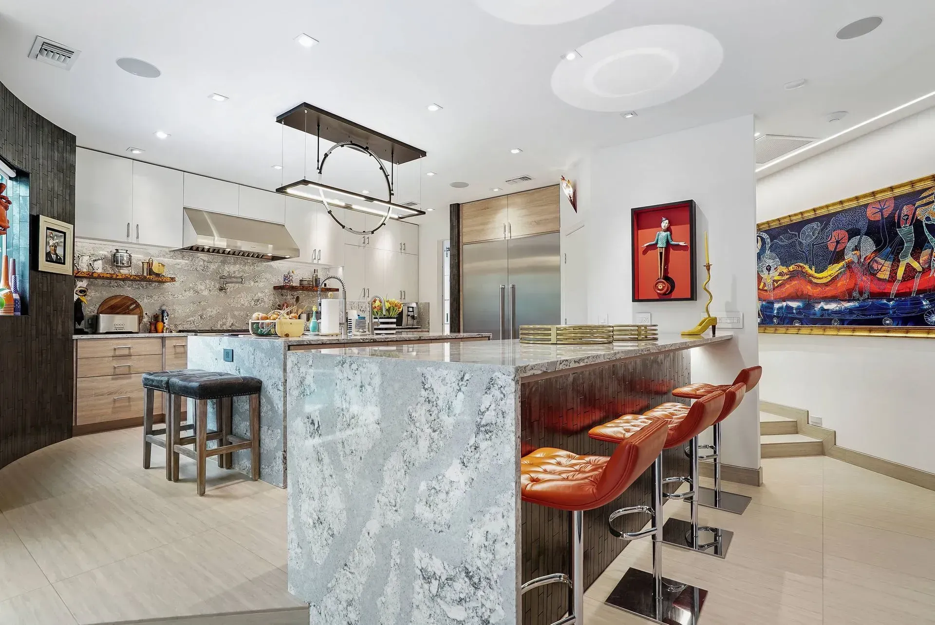 Modern kitchen with marble island, red bar stools, and colorful wall art