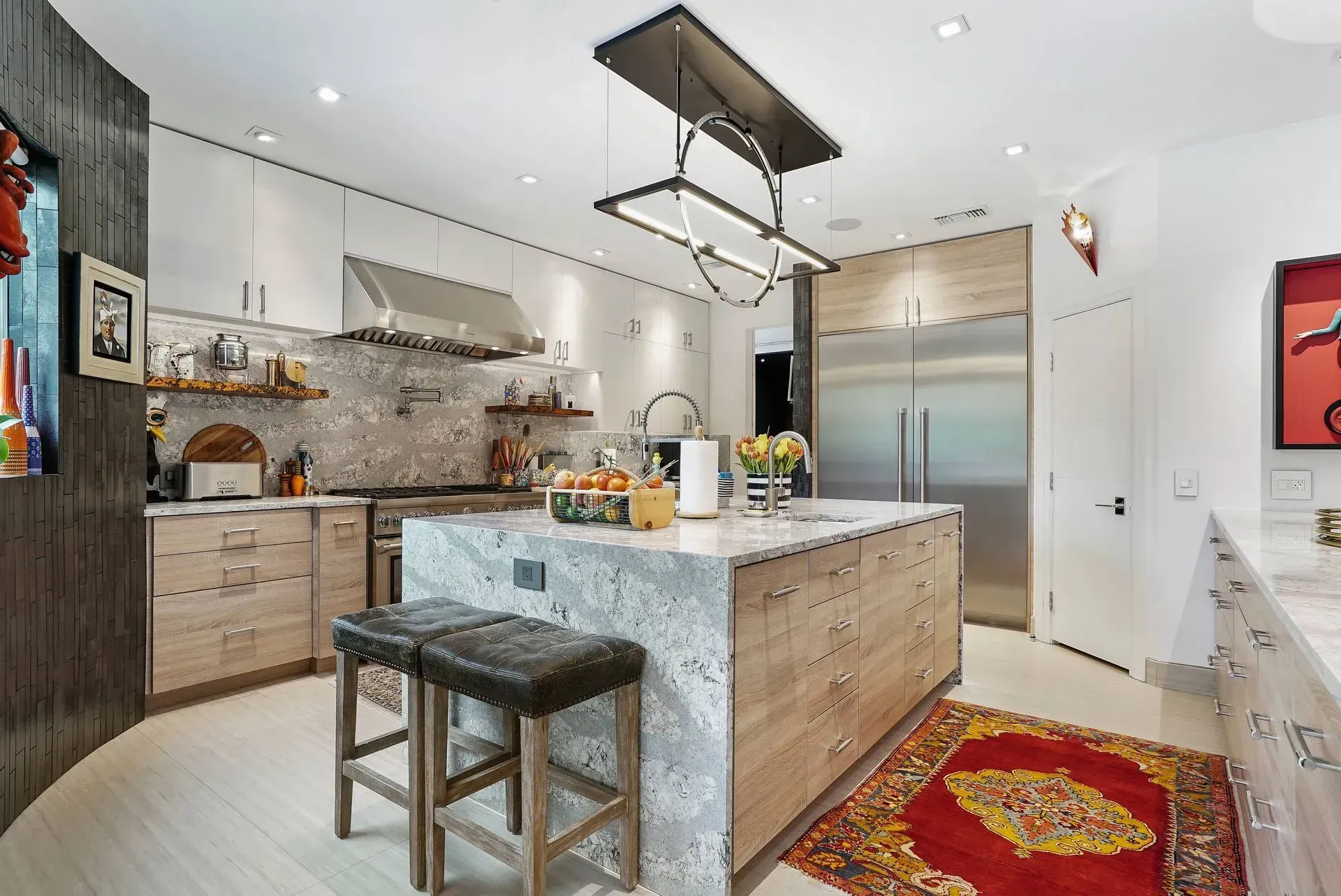 Bright modern kitchen with a marble island, stainless appliances, and red patterned rug.
