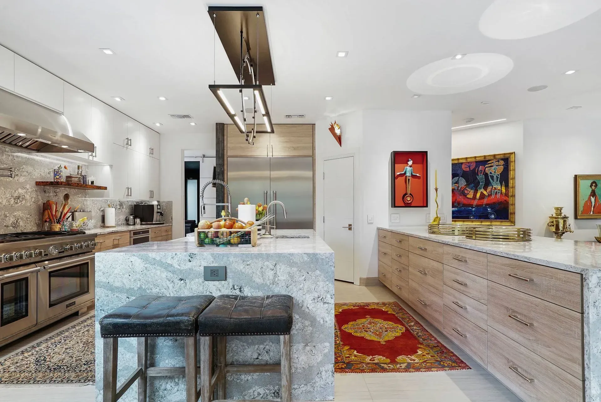 Bright modern kitchen with marble island, black stools, stainless appliances, and colorful wall art