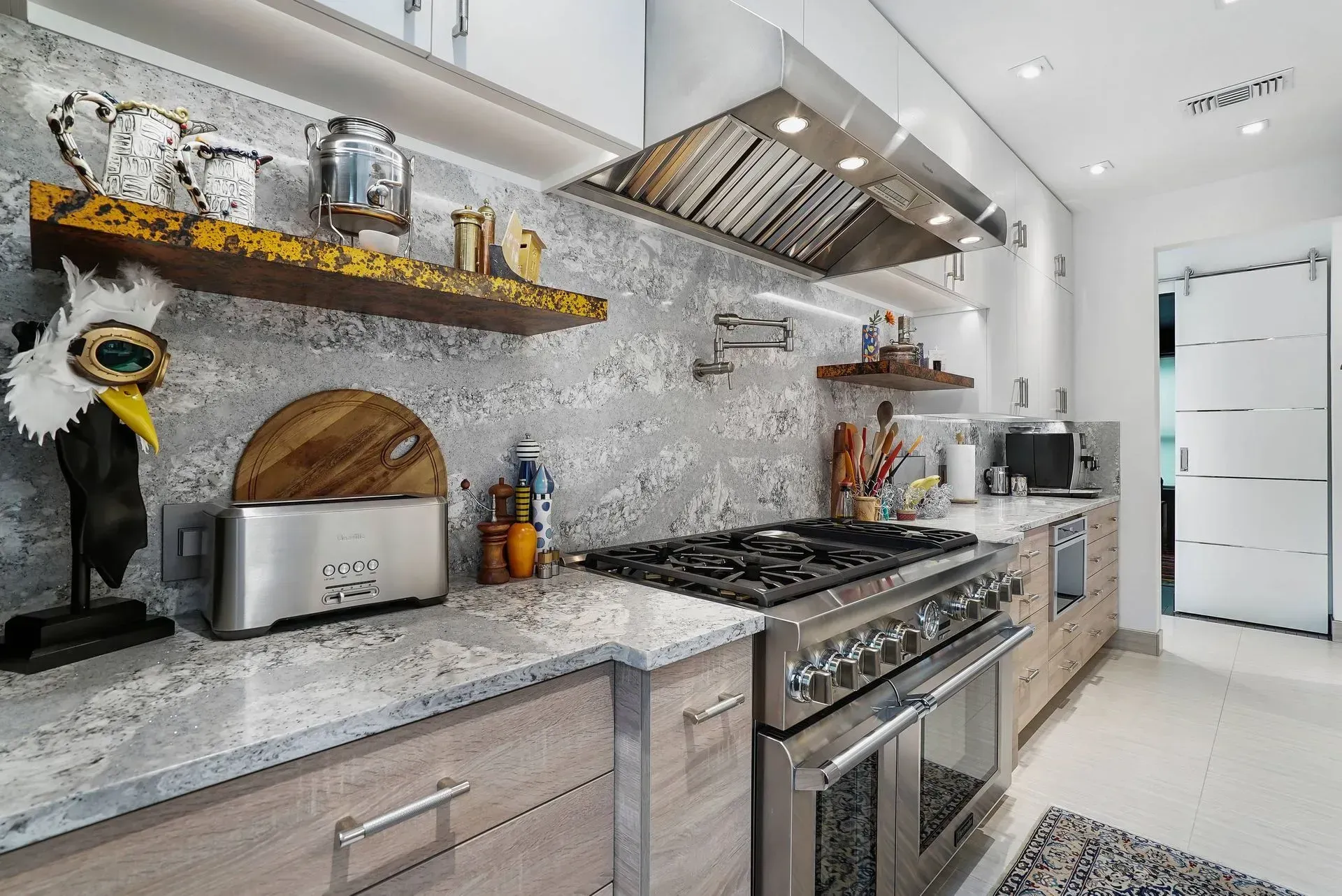 Modern kitchen with stainless steel appliances, gray marble backsplash, and white cabinetry