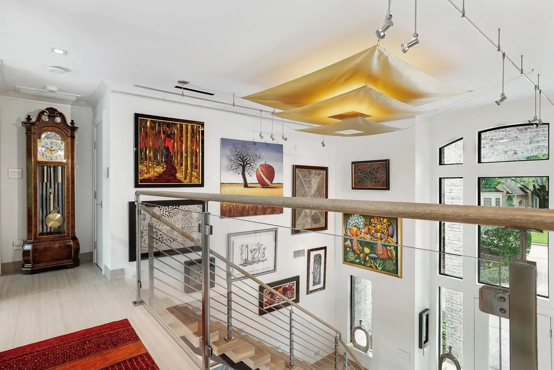 Bright modern foyer with staircase, glass railing, wall art, large clock, and hanging geometric light fixture