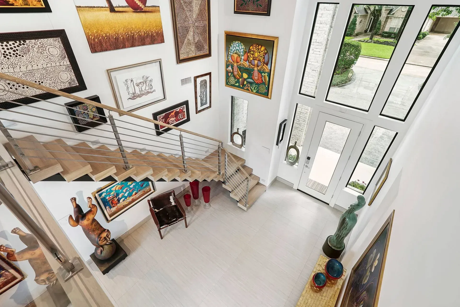 Bright art-filled foyer with staircase, white walls, large windows, and a small table and chairs below.