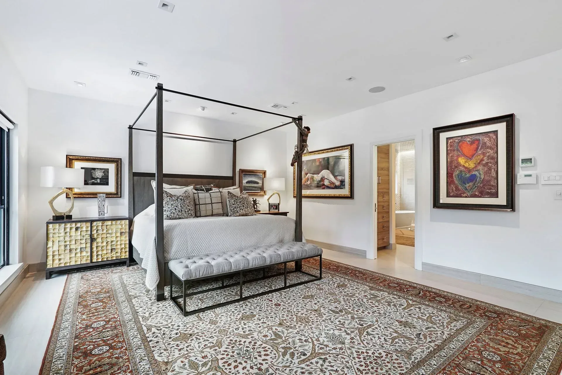 Bright bedroom with a four-poster bed, patterned rug, and framed wall art
