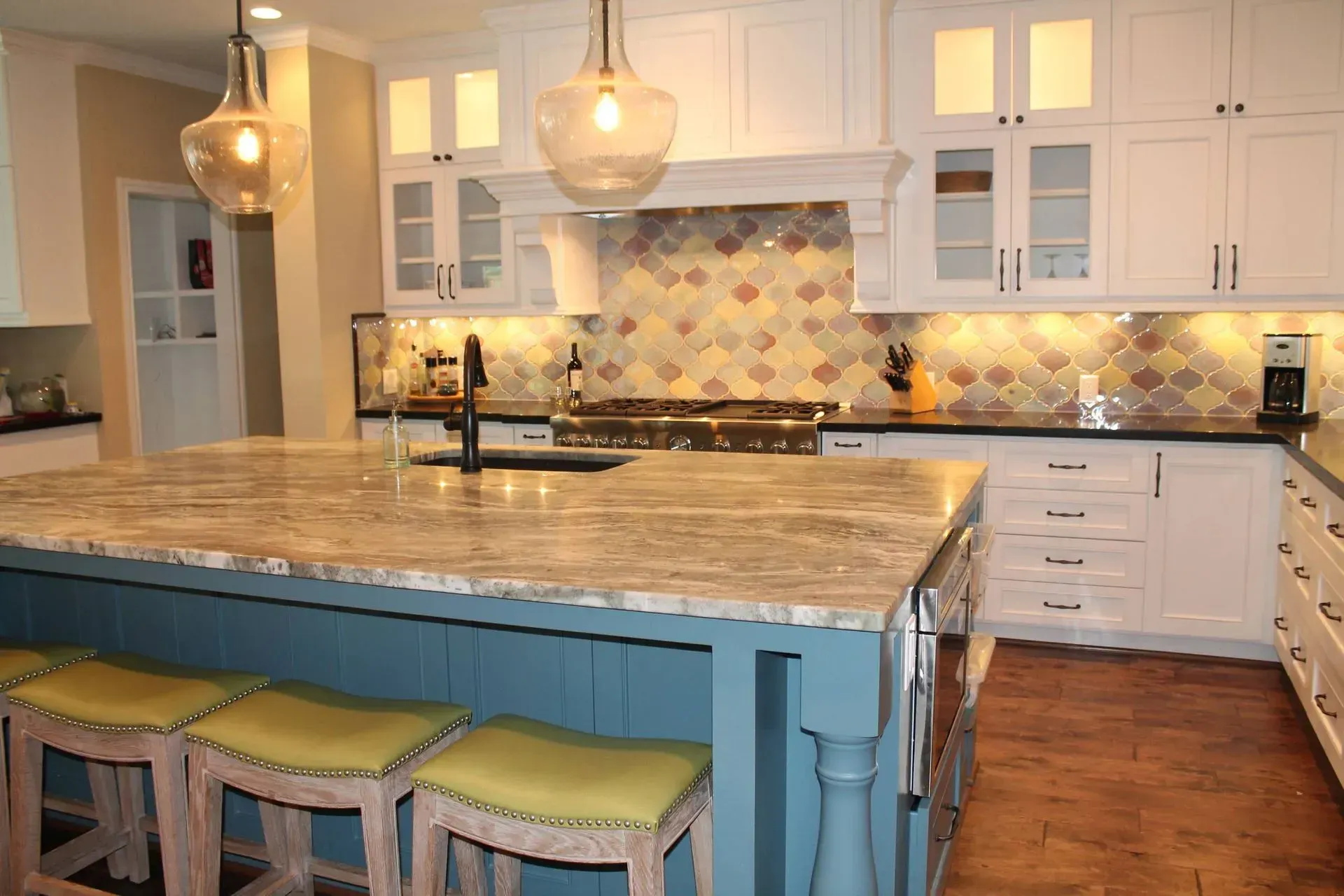Modern kitchen with marble island, blue base cabinets, white cupboards, pendant lights, and patterned backsplash