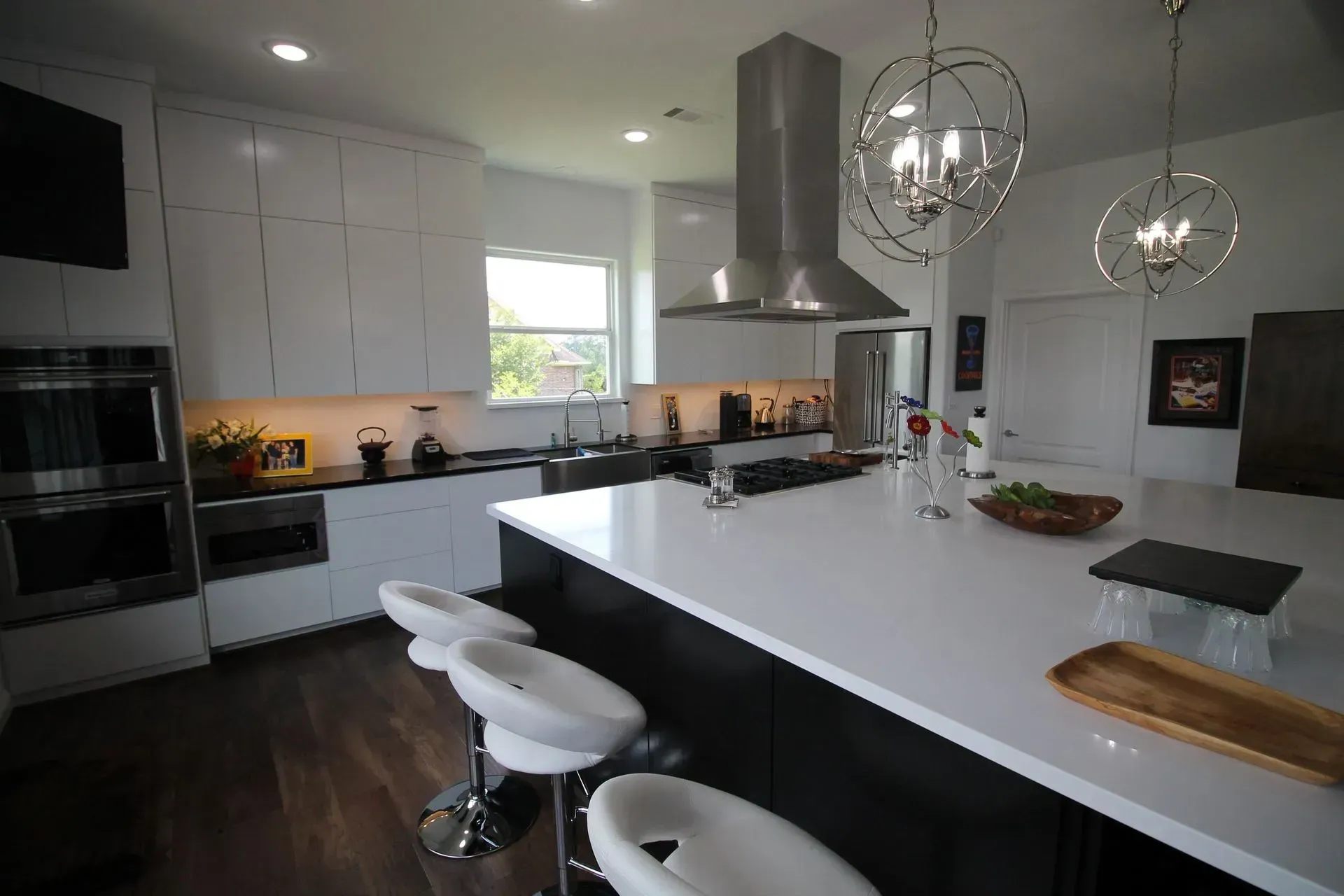 Modern white kitchen with island, bar stools, pendant lights, and dark wood floors