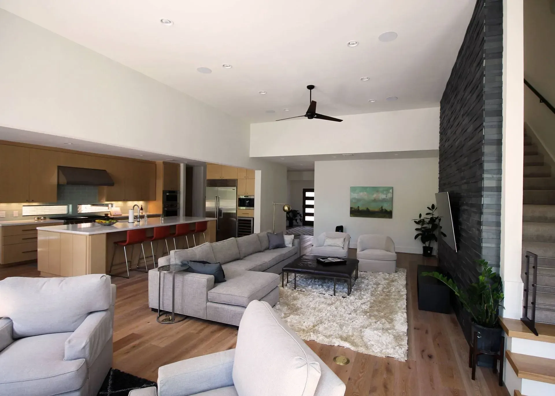 Modern open-concept living room with gray sofas, wood floors, and a kitchen bar in the background