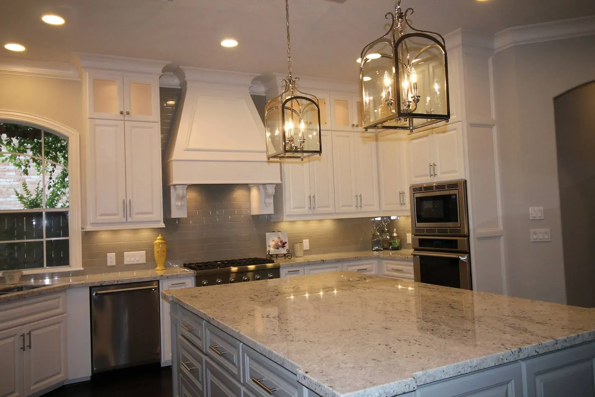 Bright modern kitchen with large granite island, white cabinets, and hanging pendant lights.