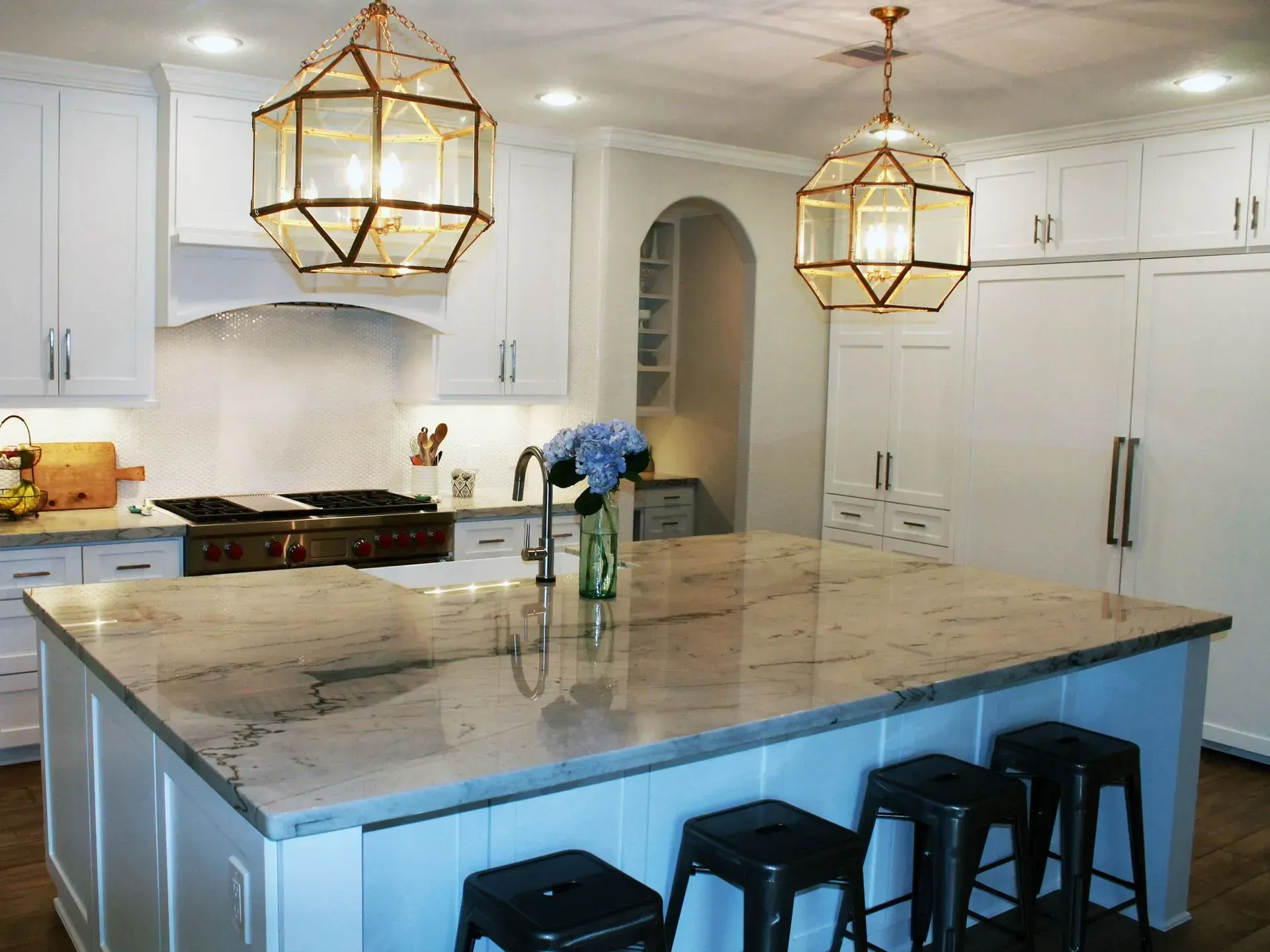 Bright white kitchen with a large marble island, gold pendant lights, and blue flowers in a vase.
