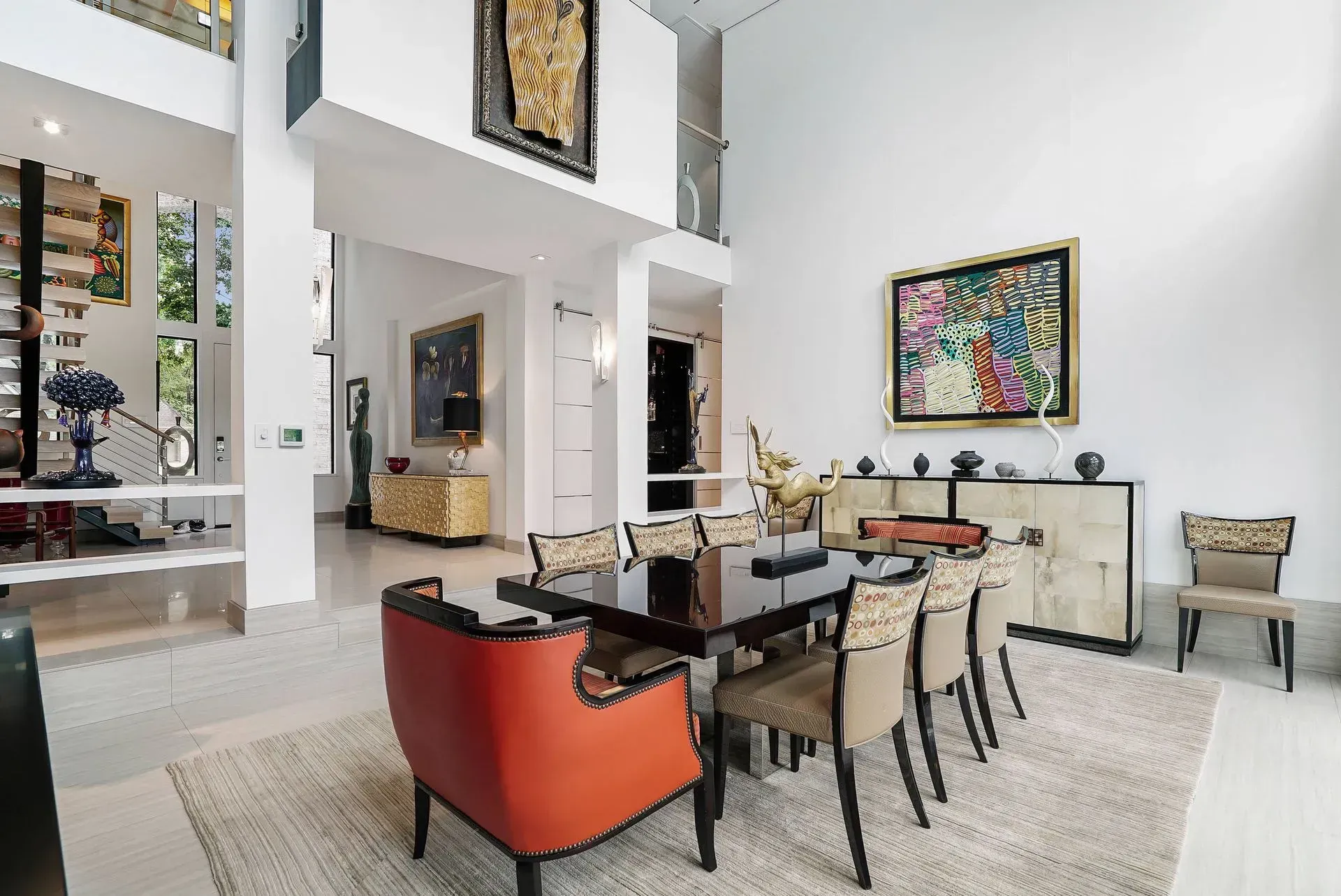 Modern living room with high ceilings, red armchairs, dining table, and colorful wall art