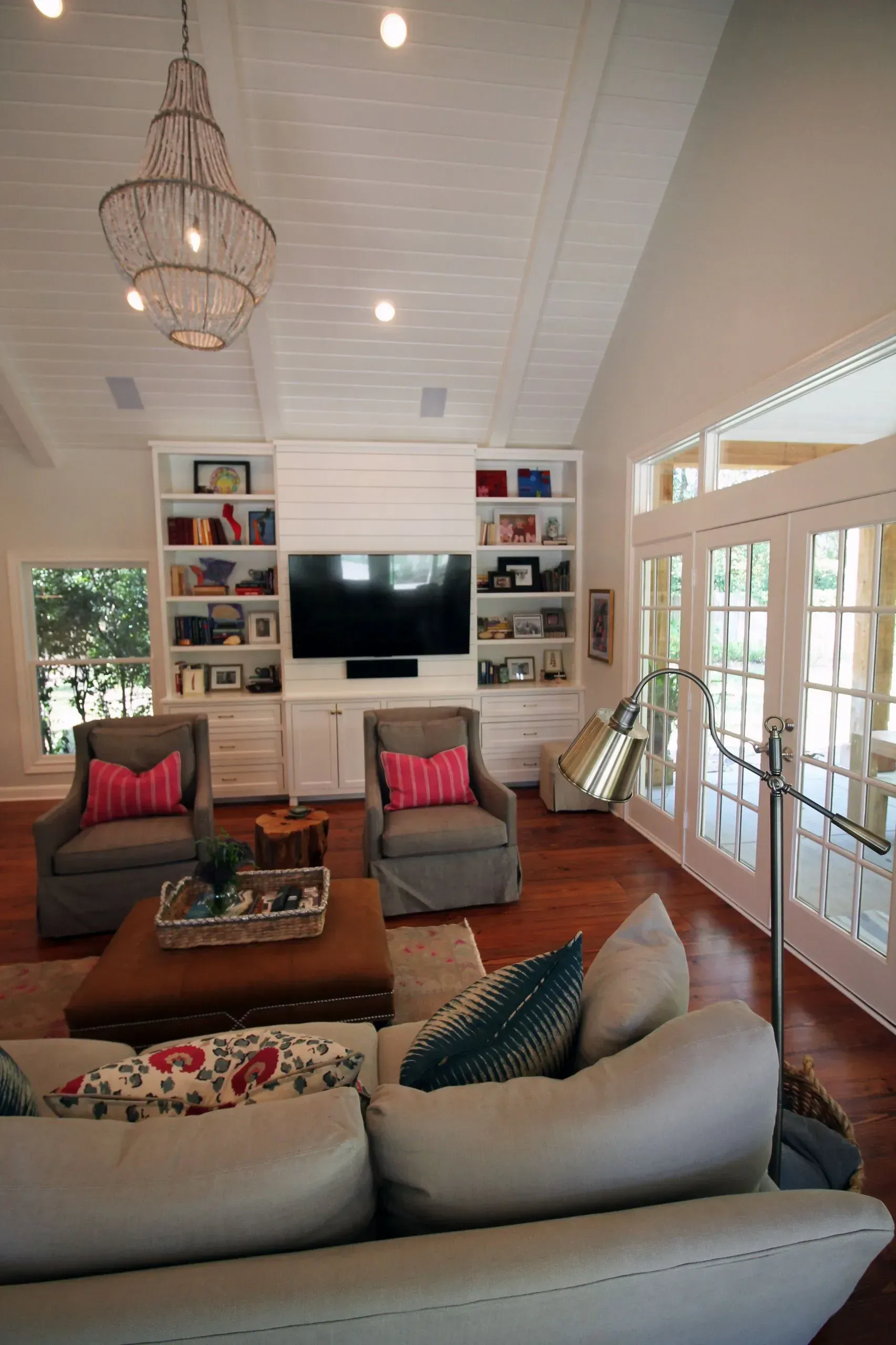 Bright living room with brown seating, built-in shelves, large TV, and French doors opening to a porch.