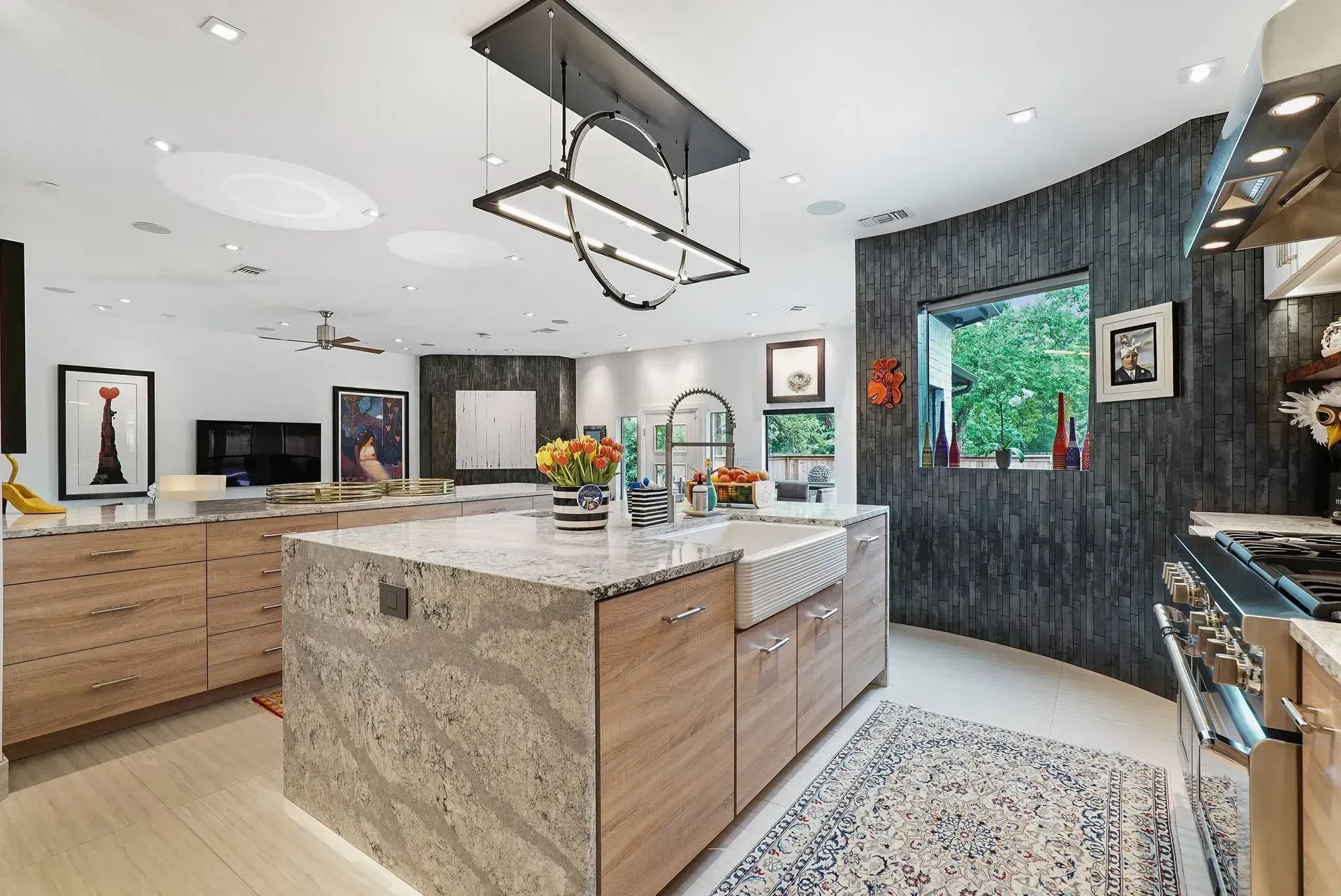 Bright modern kitchen with large island, wood cabinets, dark accent wall, and patterned rug