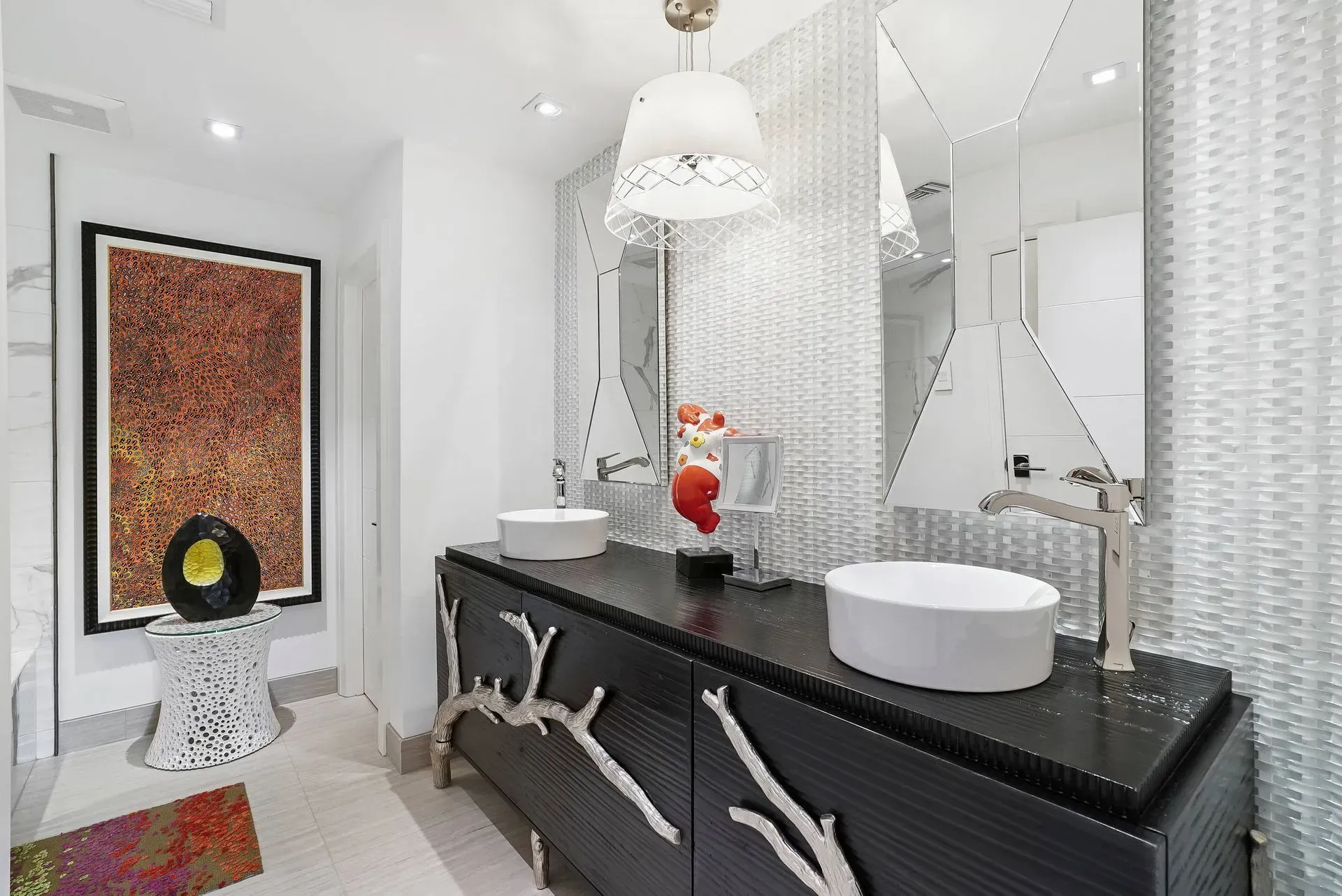 Modern white bathroom with black vanity, round sinks, mirrored wall, and pendant light