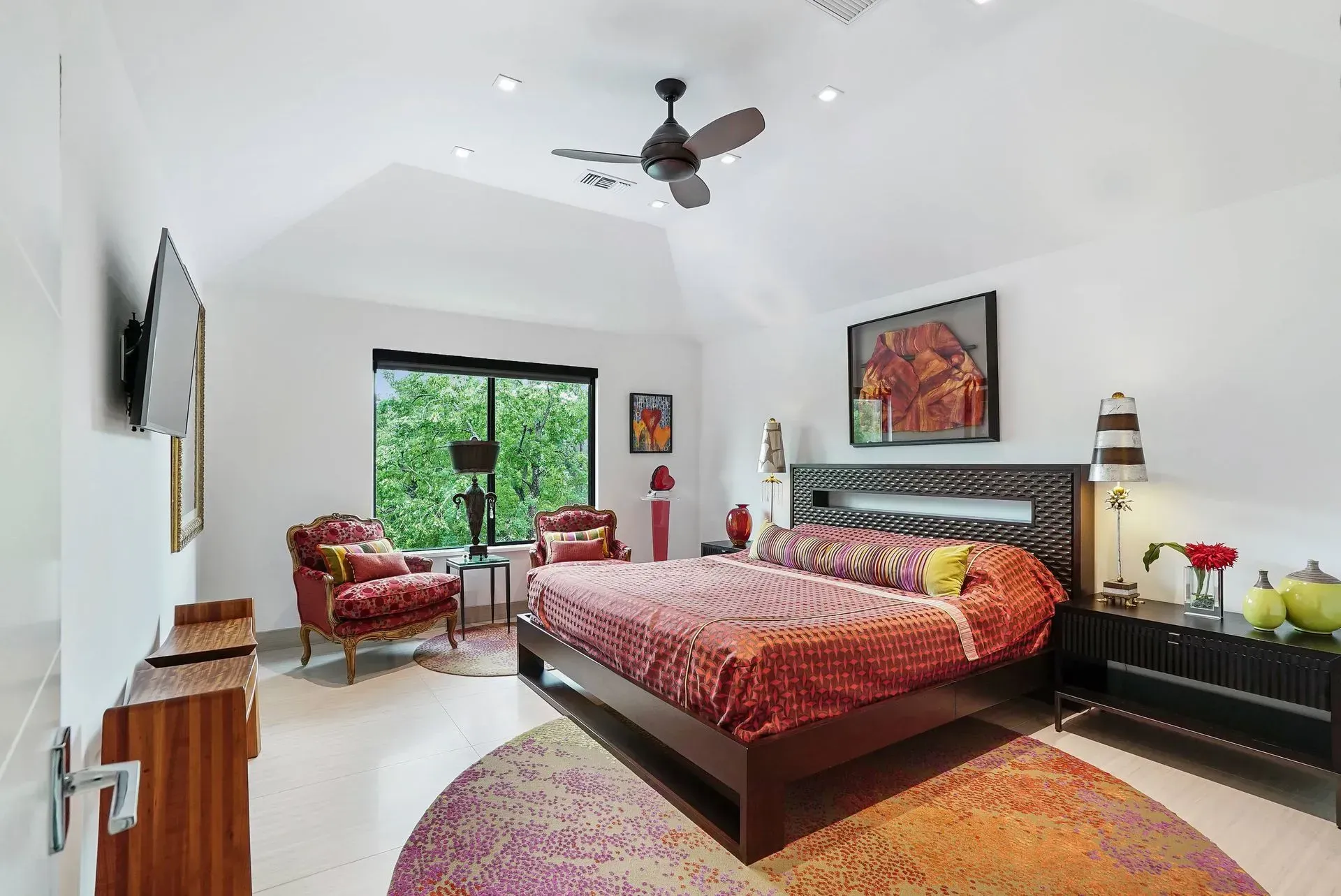 Bright bedroom with king bed, red patterned bedding, balcony doors, and a ceiling fan