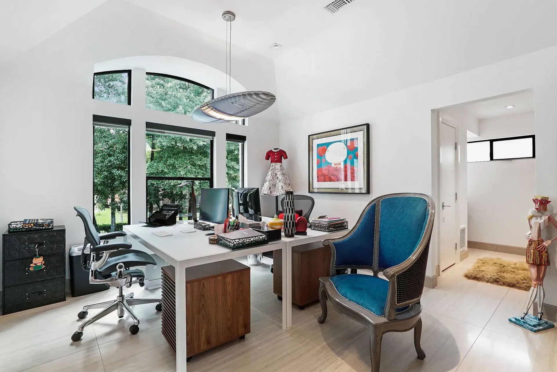 Bright home office with white desk, blue chair, large windows, and colorful wall art
