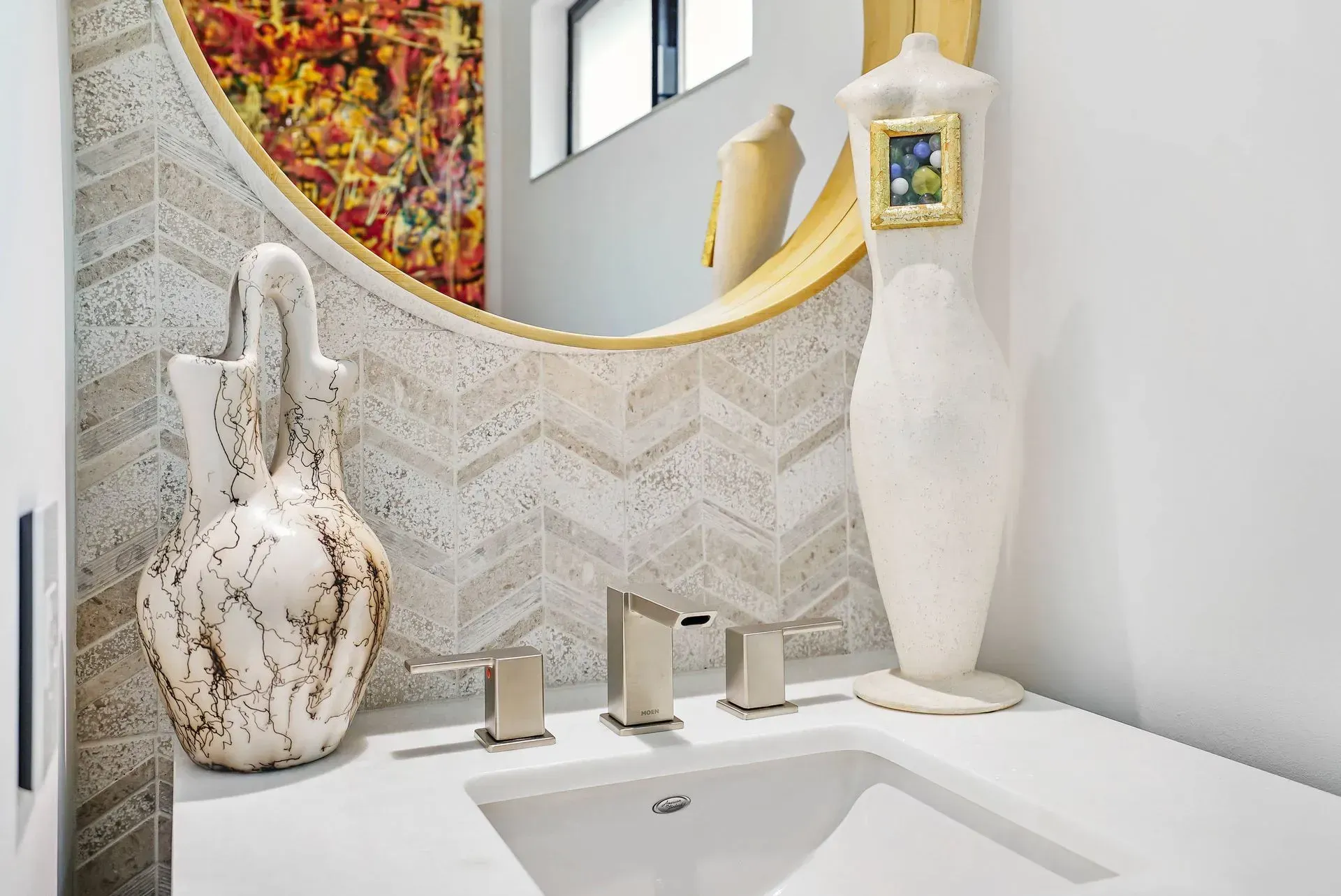 Modern bathroom sink with white and gold decor, sculptural vases, and colorful mosaic wall accent