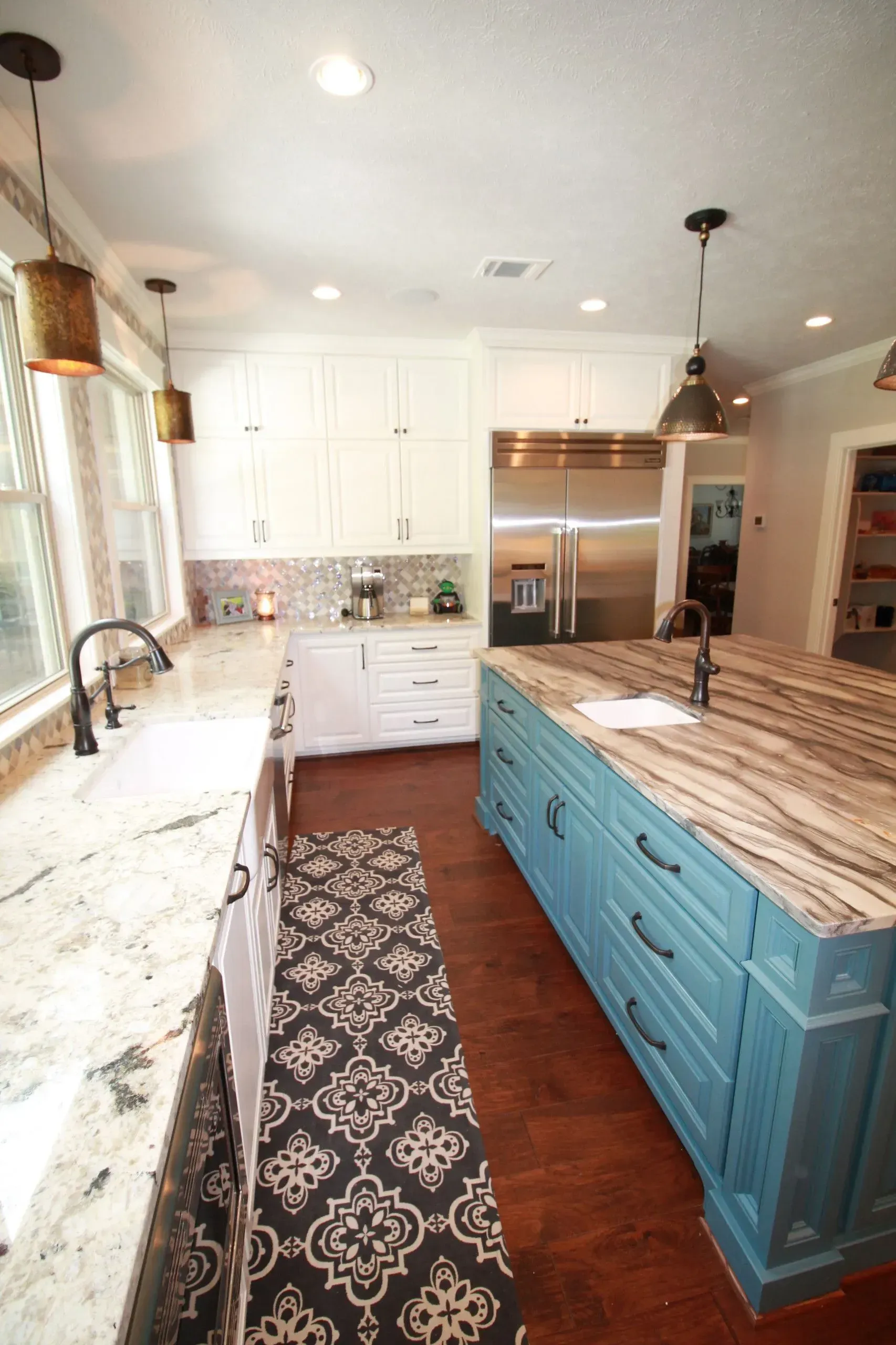 Bright kitchen with blue island, white cabinets, patterned runner, and stainless steel appliances.
