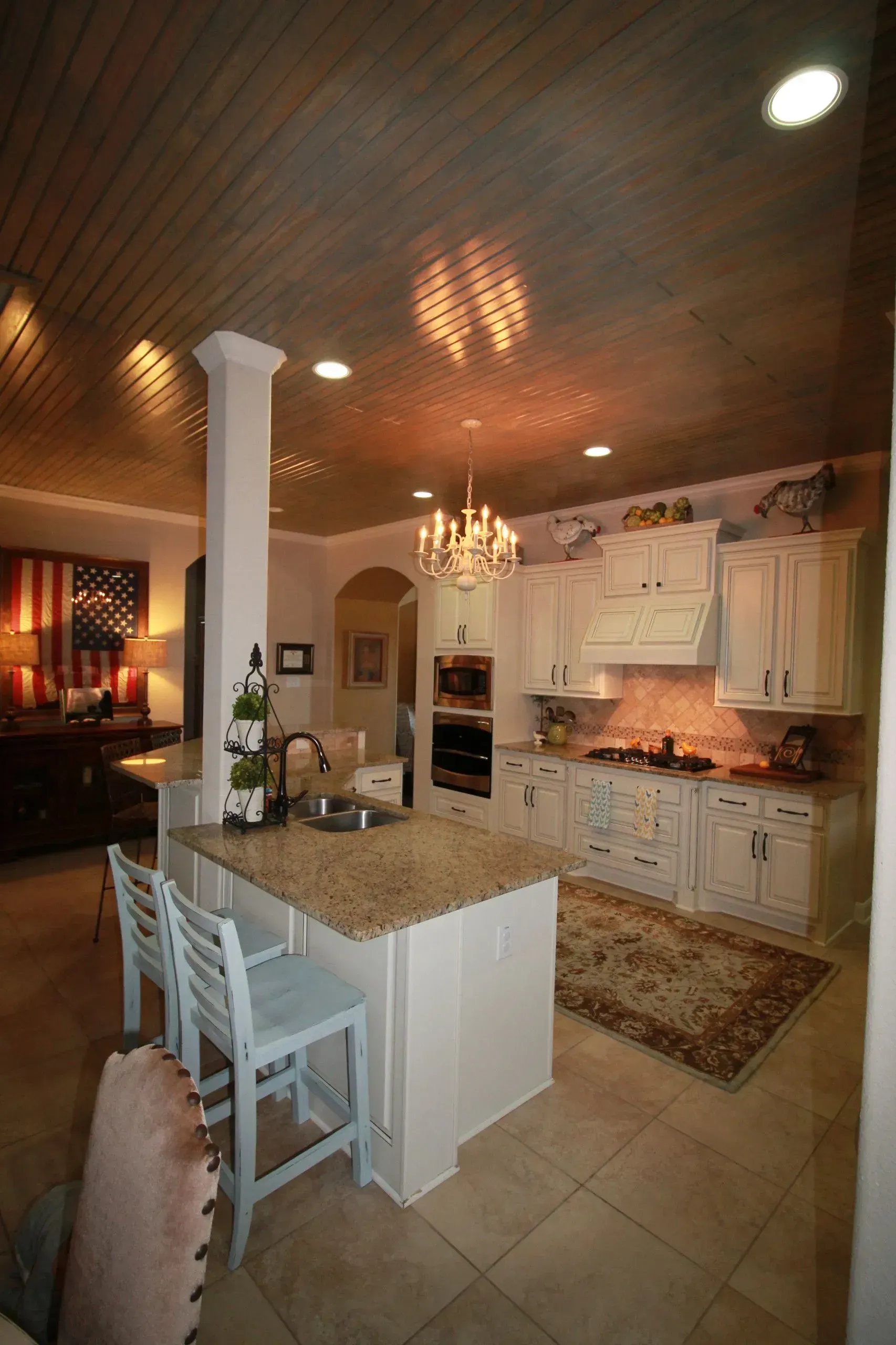 Elegant kitchen with white cabinets, granite island, tiled floor, and warm wood ceiling lighting
