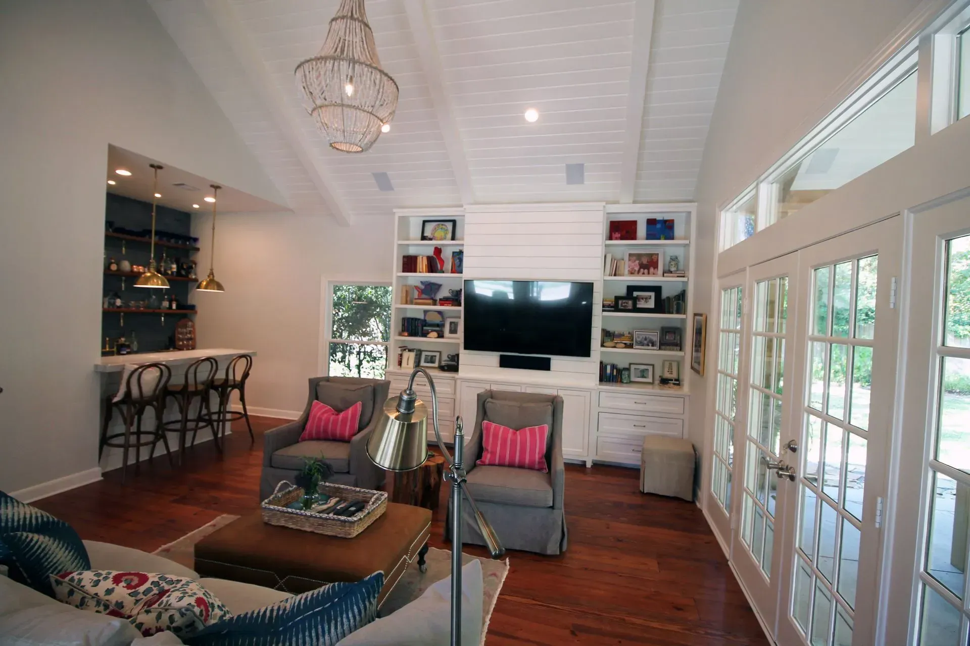 Bright living room with gray chairs, pink pillows, TV, wooden coffee table, and French doors to a patio