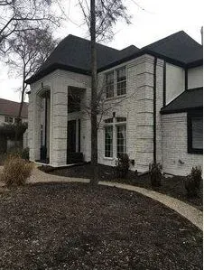 Two-story white brick house with black roof and arched front entry in a landscaped yard