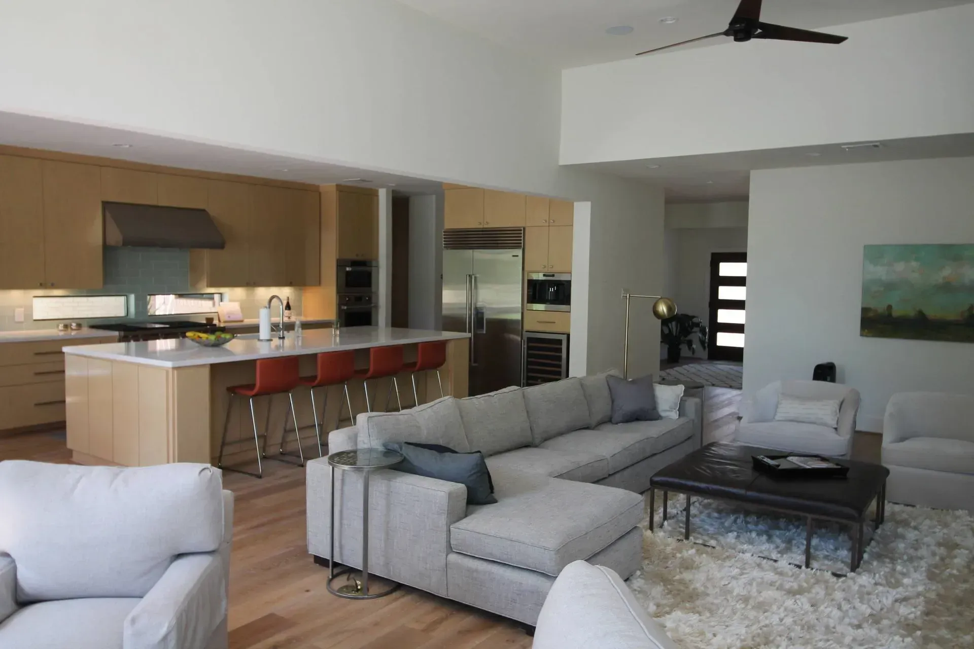 Modern open-plan living room with gray sectional sofa, coffee table, kitchen island, and wood flooring