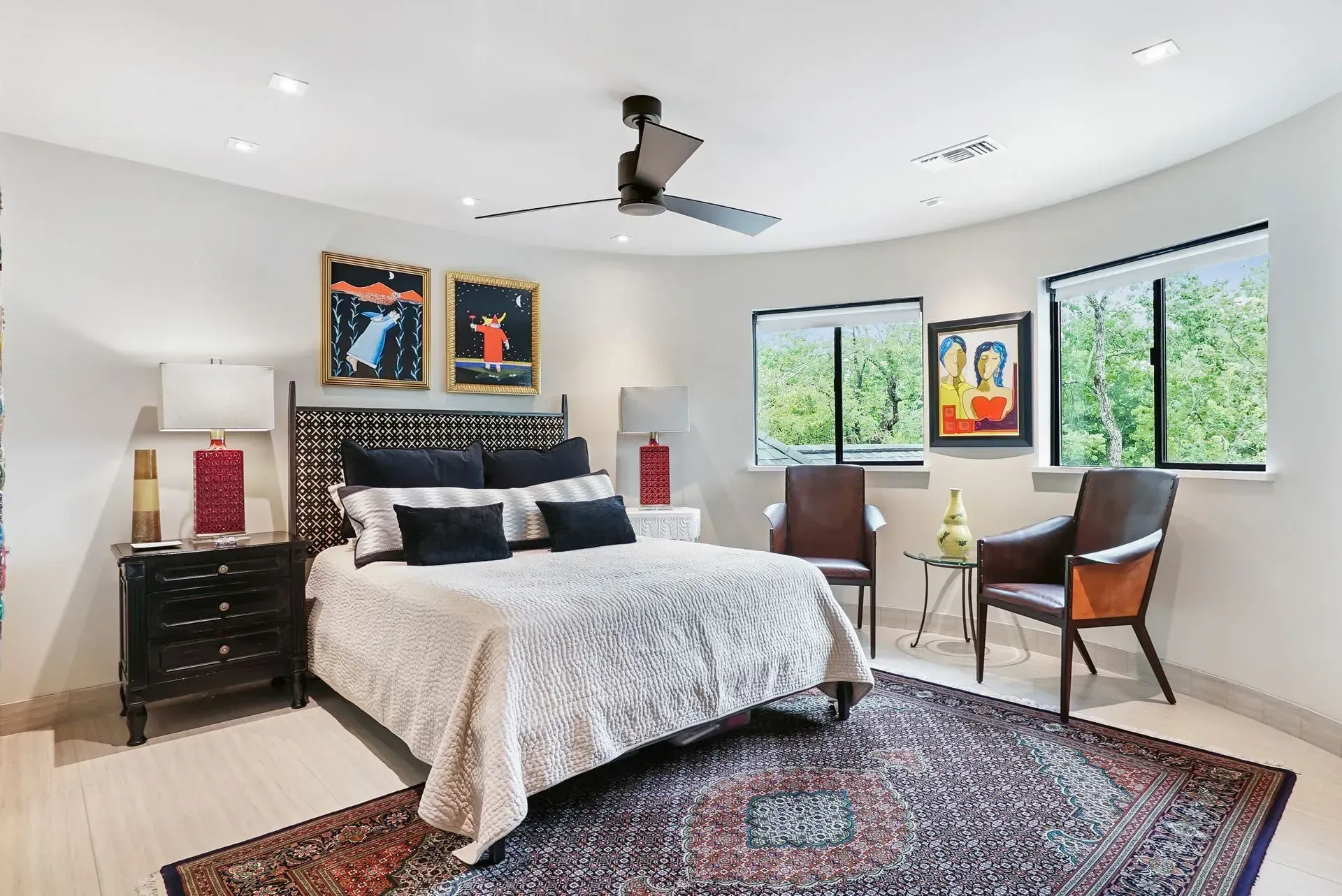 Bright bedroom with a bed, patterned rug, desk chair, and large windows overlooking greenery