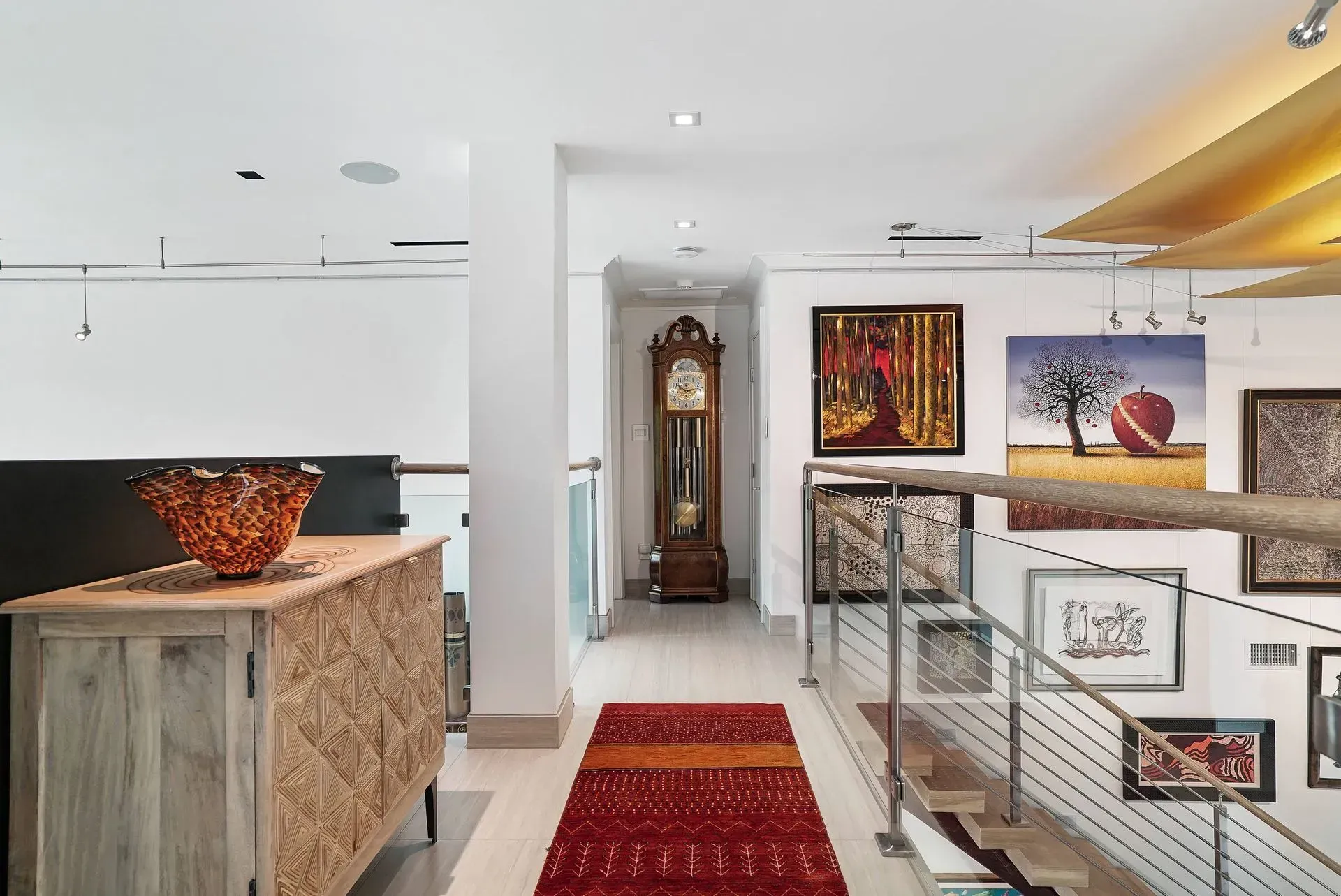 Bright modern hallway with red runner, wall art, grandfather clock, and open stair railing