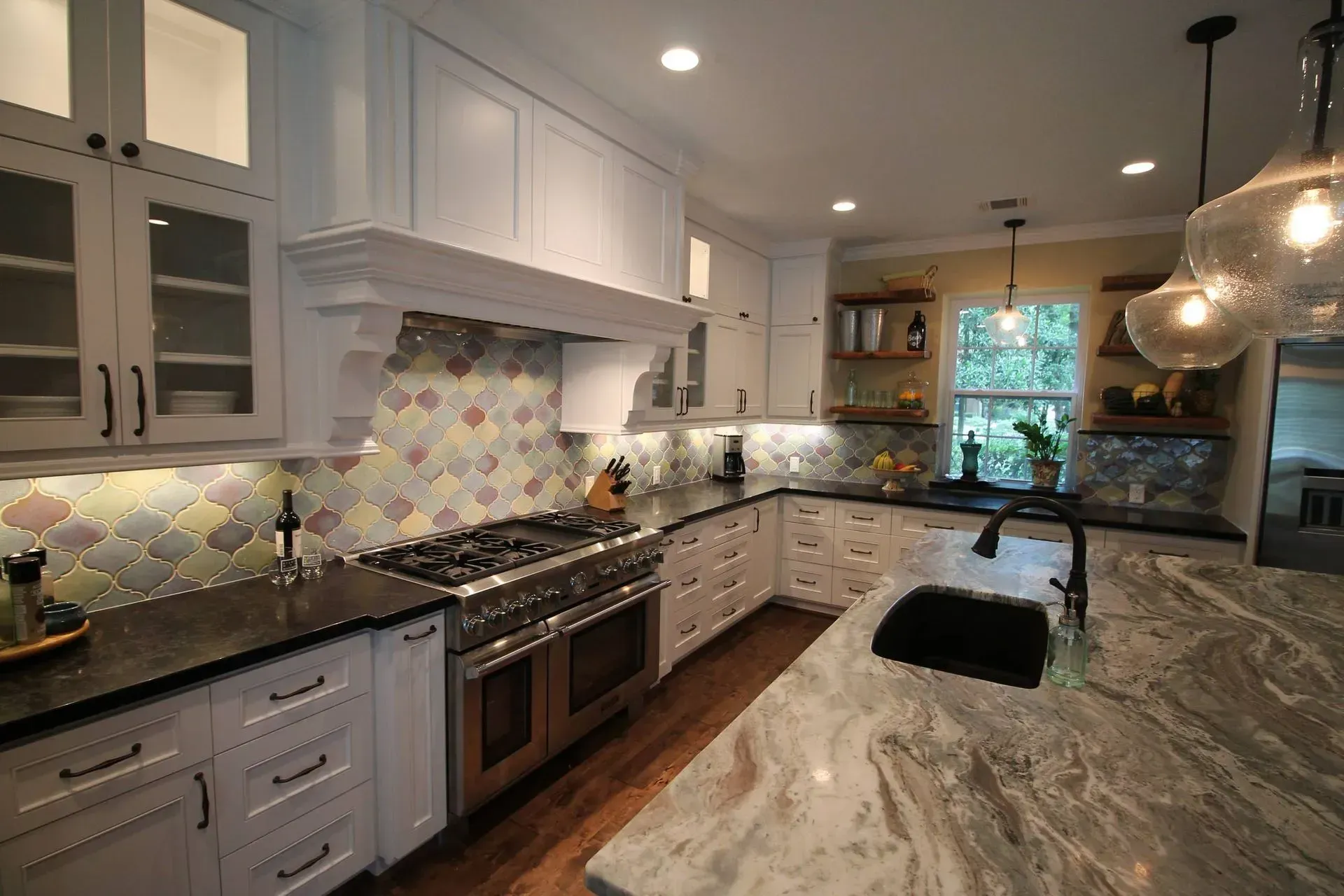 Bright modern kitchen with white cabinets, marble island, stainless stove, and pendant lights