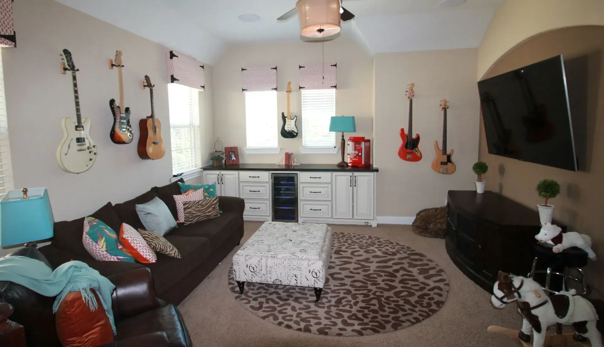 Cozy living room with couch, coffee table, wall-mounted TV, guitars, and white cabinets by windows