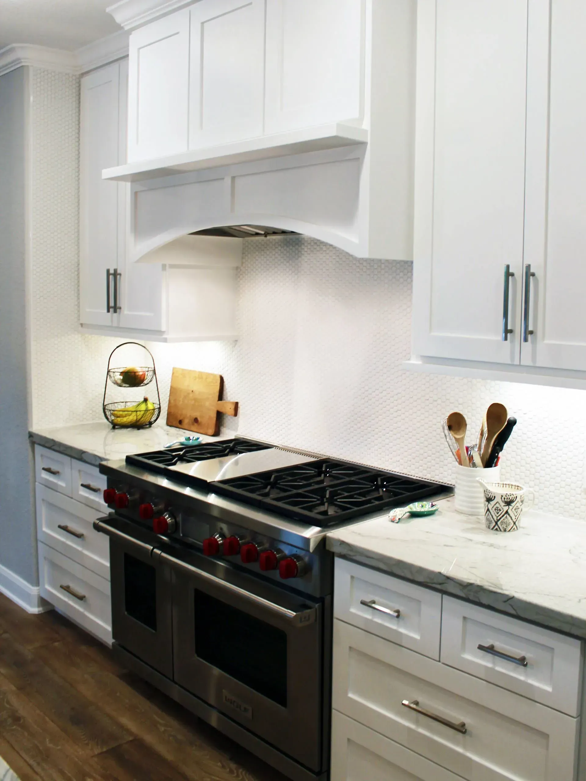Bright white kitchen with stainless steel range, marble countertop, and dark wood floor
