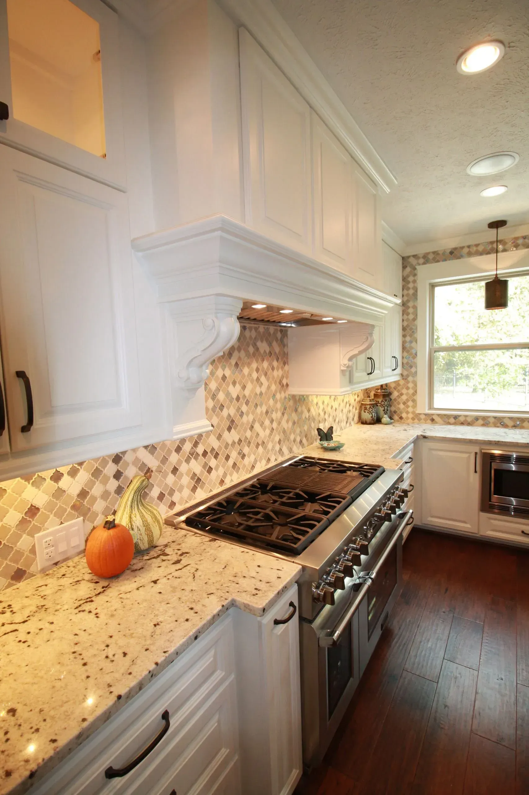Bright white kitchen with speckled countertops, gas range, mosaic backsplash, and a pumpkin on the counter.