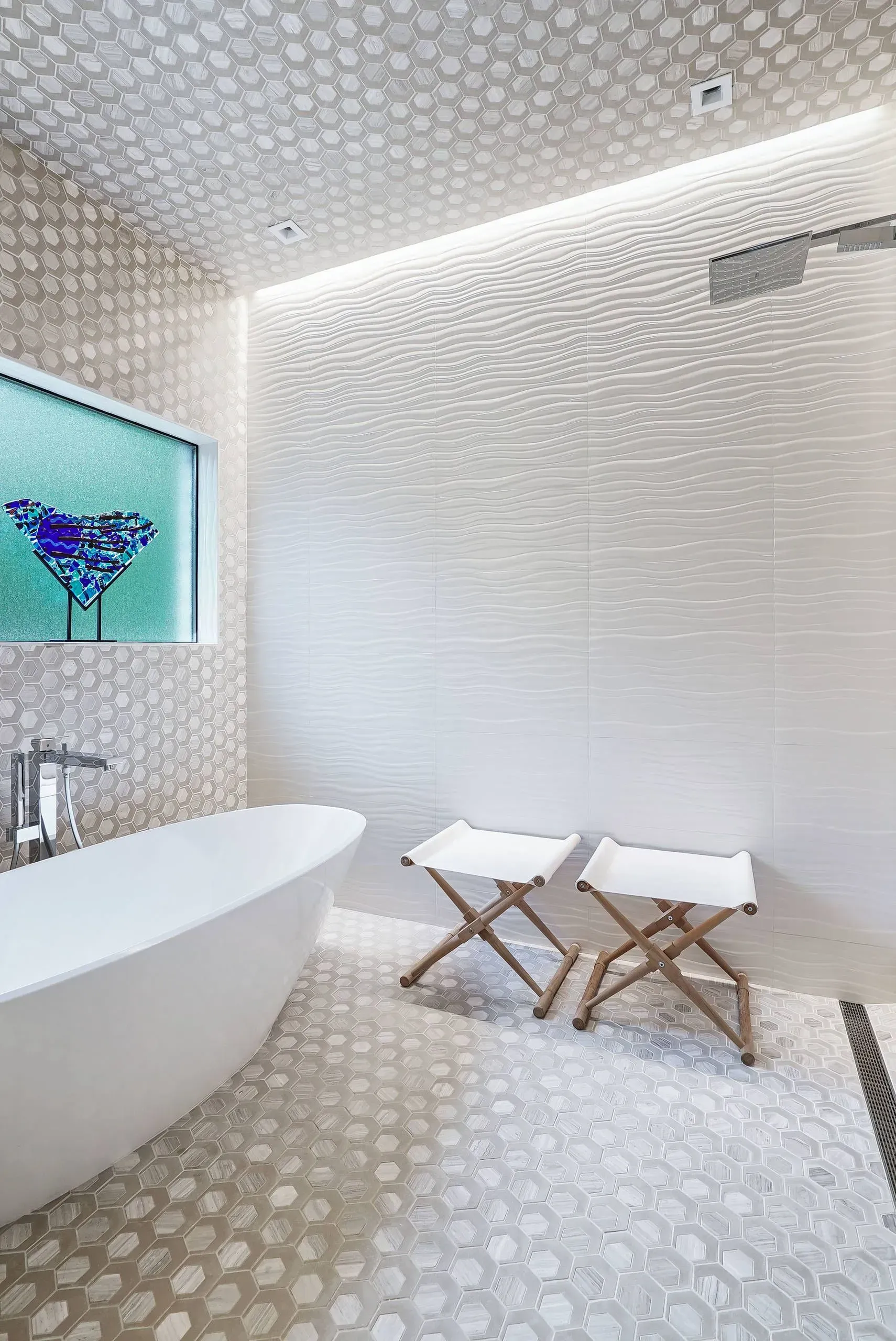 Bright white bathroom with freestanding tub, mosaic tile, wall art, and two wooden stools