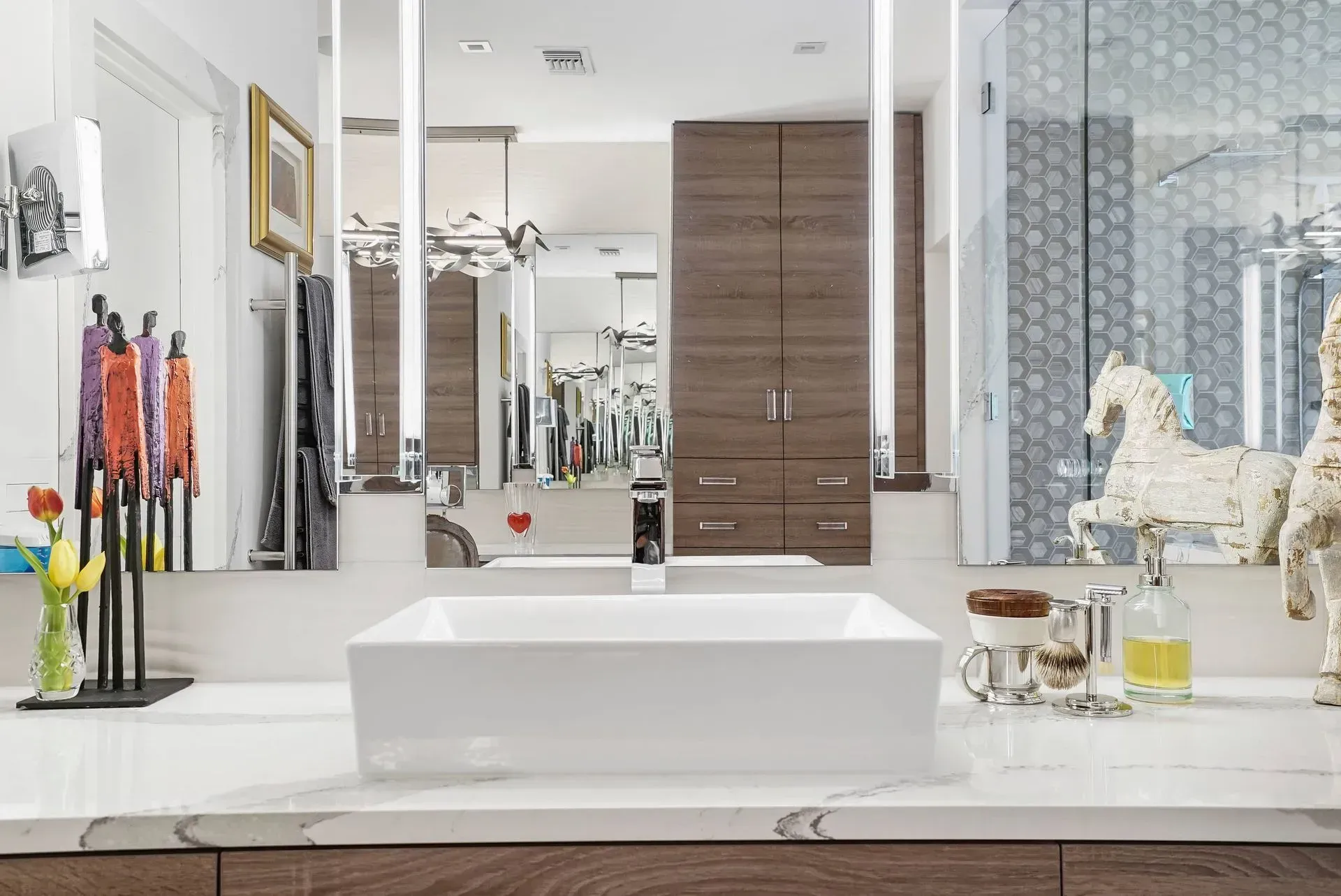 Bright modern bathroom vanity with white sink, wood cabinets, mirrors, and decorative items