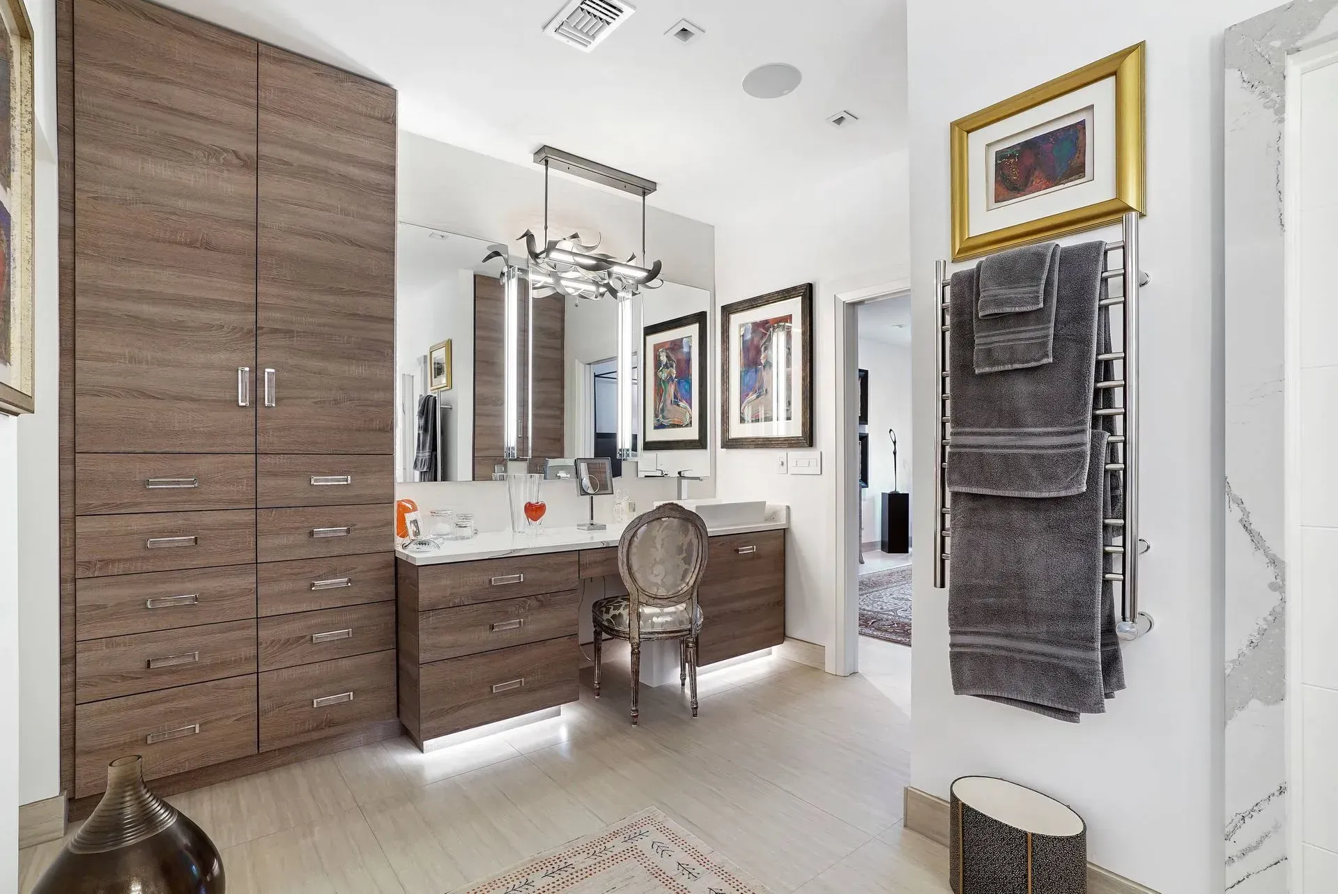 Bright bathroom with double vanity, large mirror, wood cabinets, and towels on a wall rack.