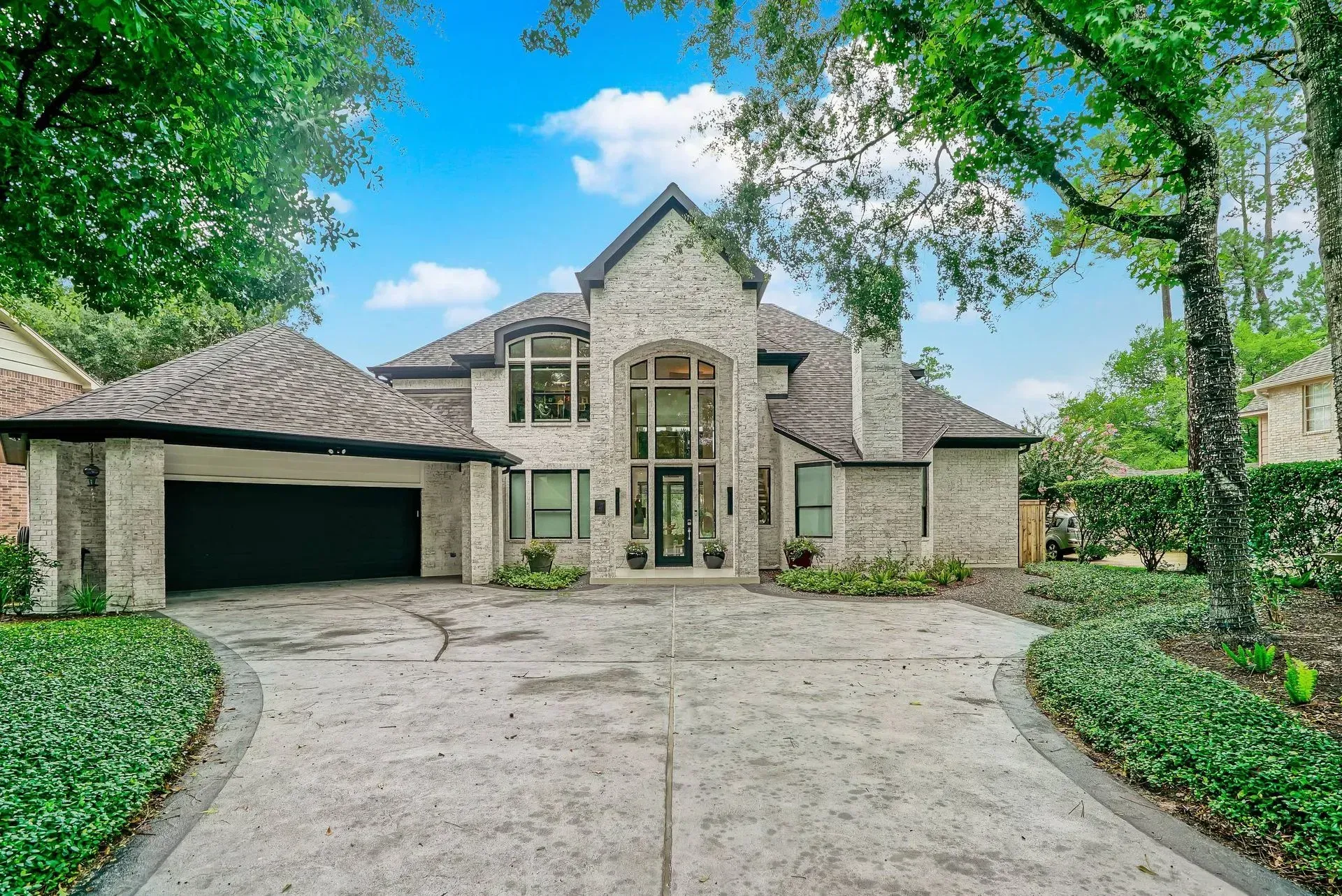 Stone house with a two-car garage and curved driveway, framed by green trees and landscaping