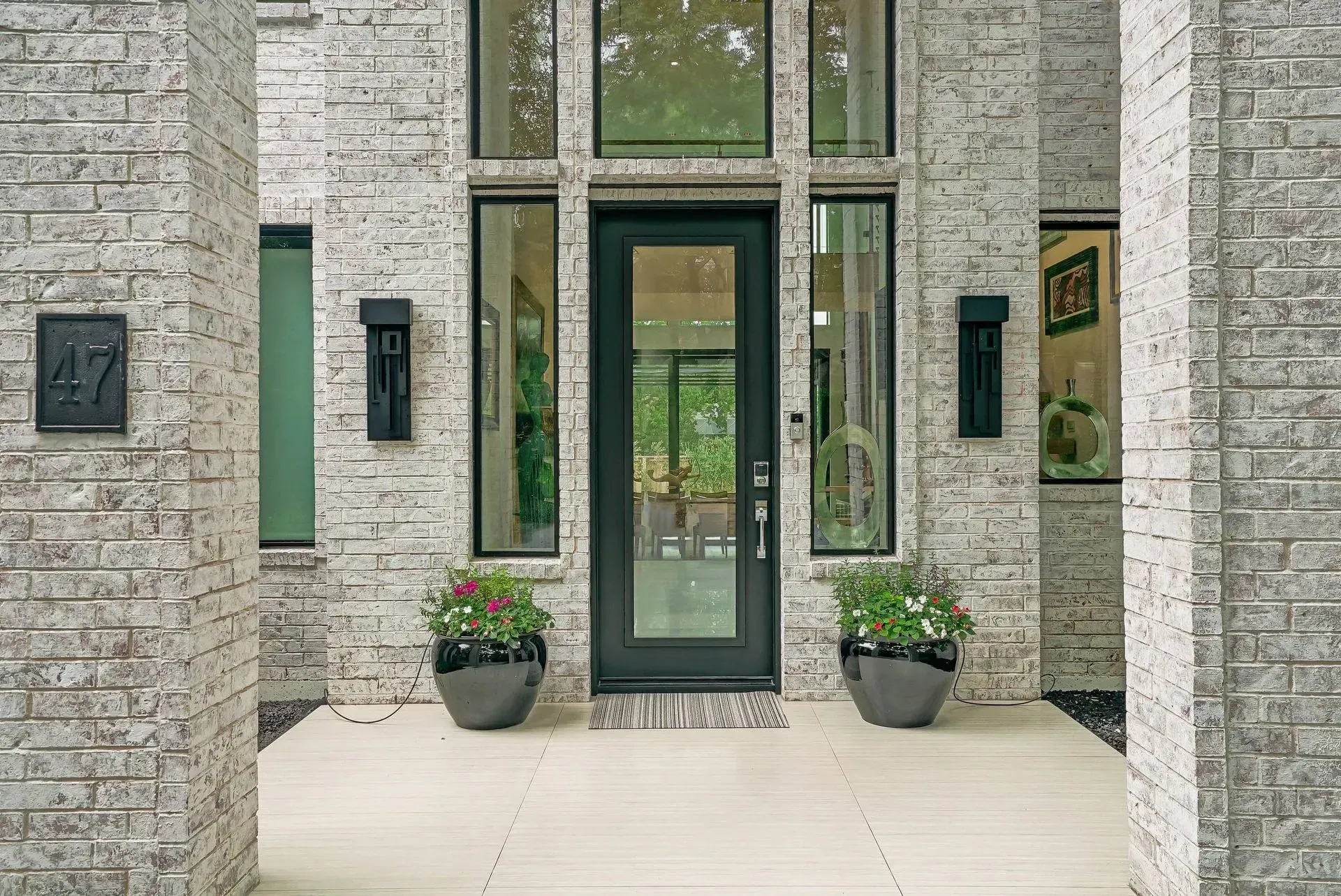 Modern stone house entrance with glass door, tall windows, and potted plants on a front walkway