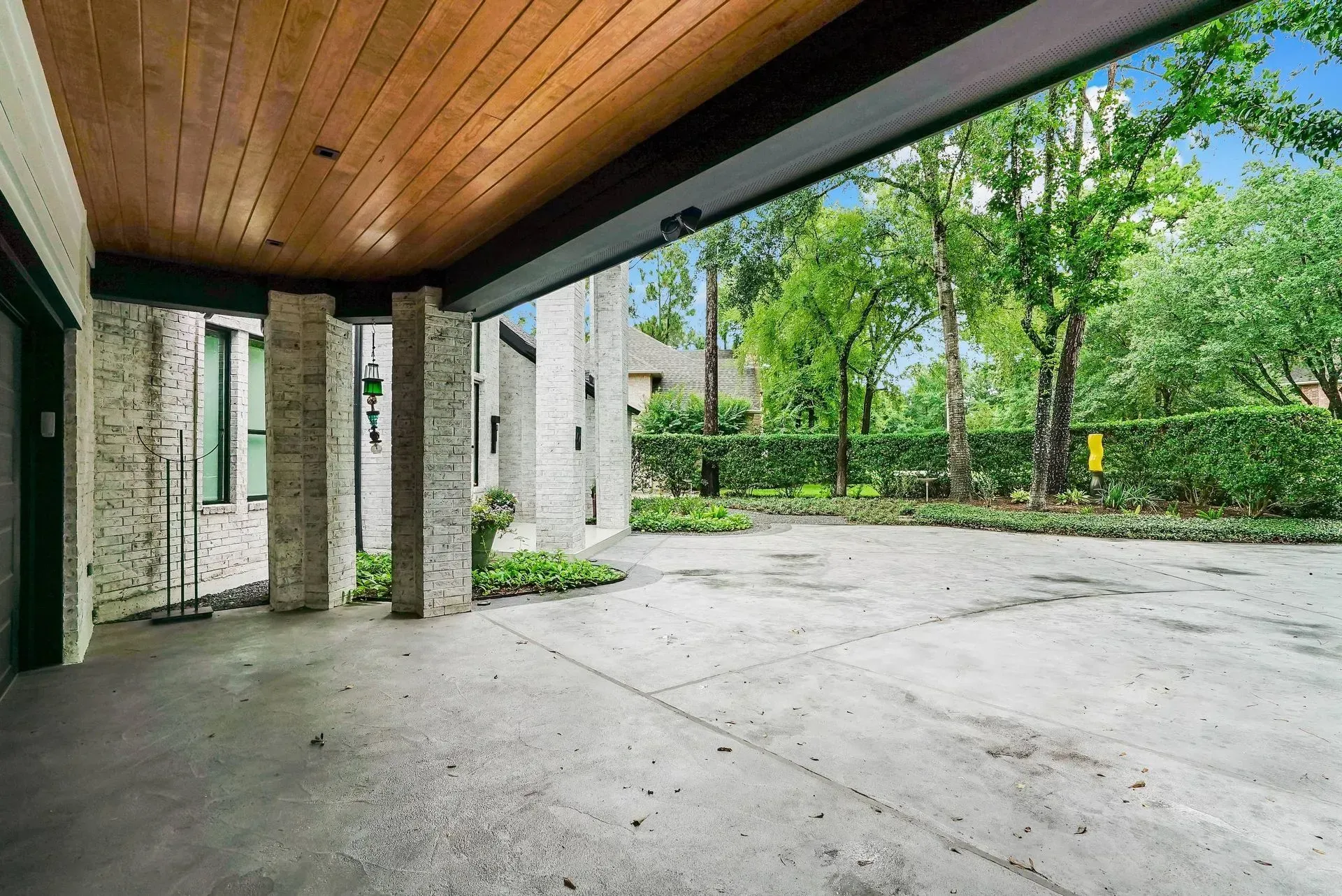 Covered concrete patio with stone columns, wood ceiling, and view of a green backyard.