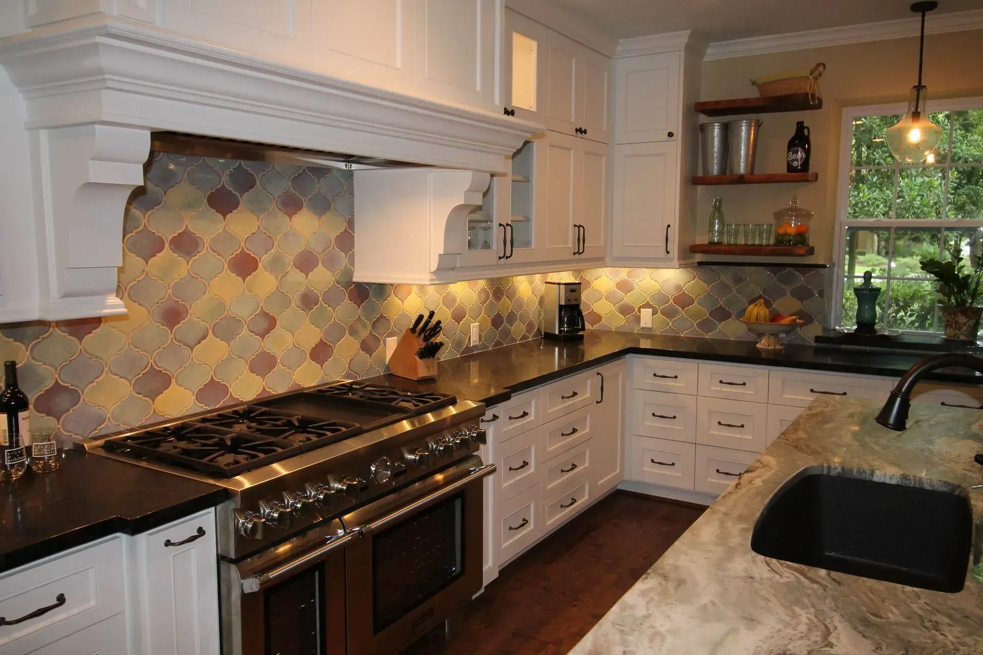 Bright modern kitchen with white cabinets, black counters, tiled backsplash, and a gas stove by a window.