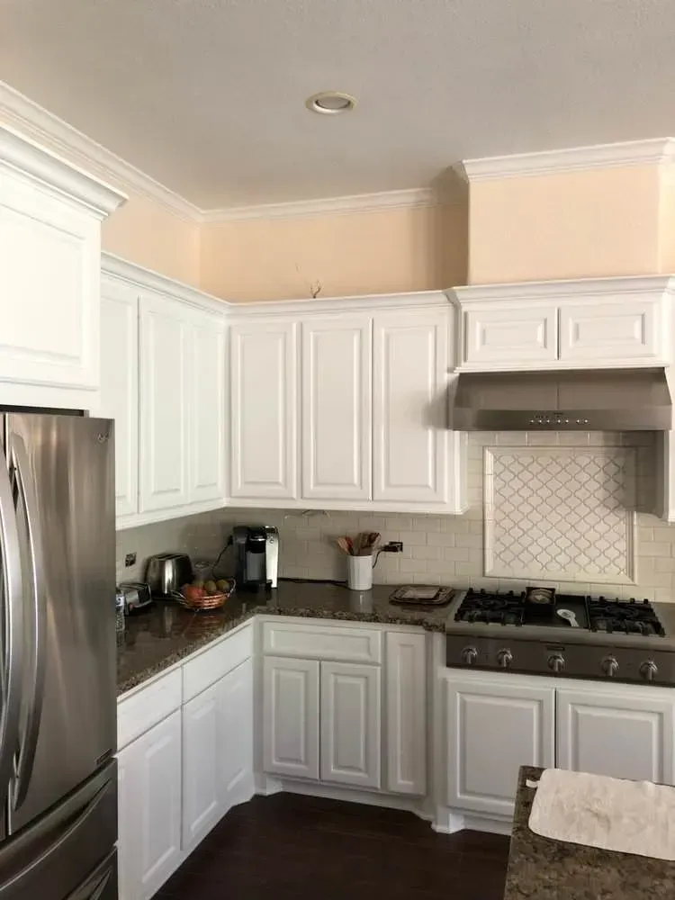 Bright white kitchen with stainless fridge, corner cabinets, gas stove, and beige tile backsplash