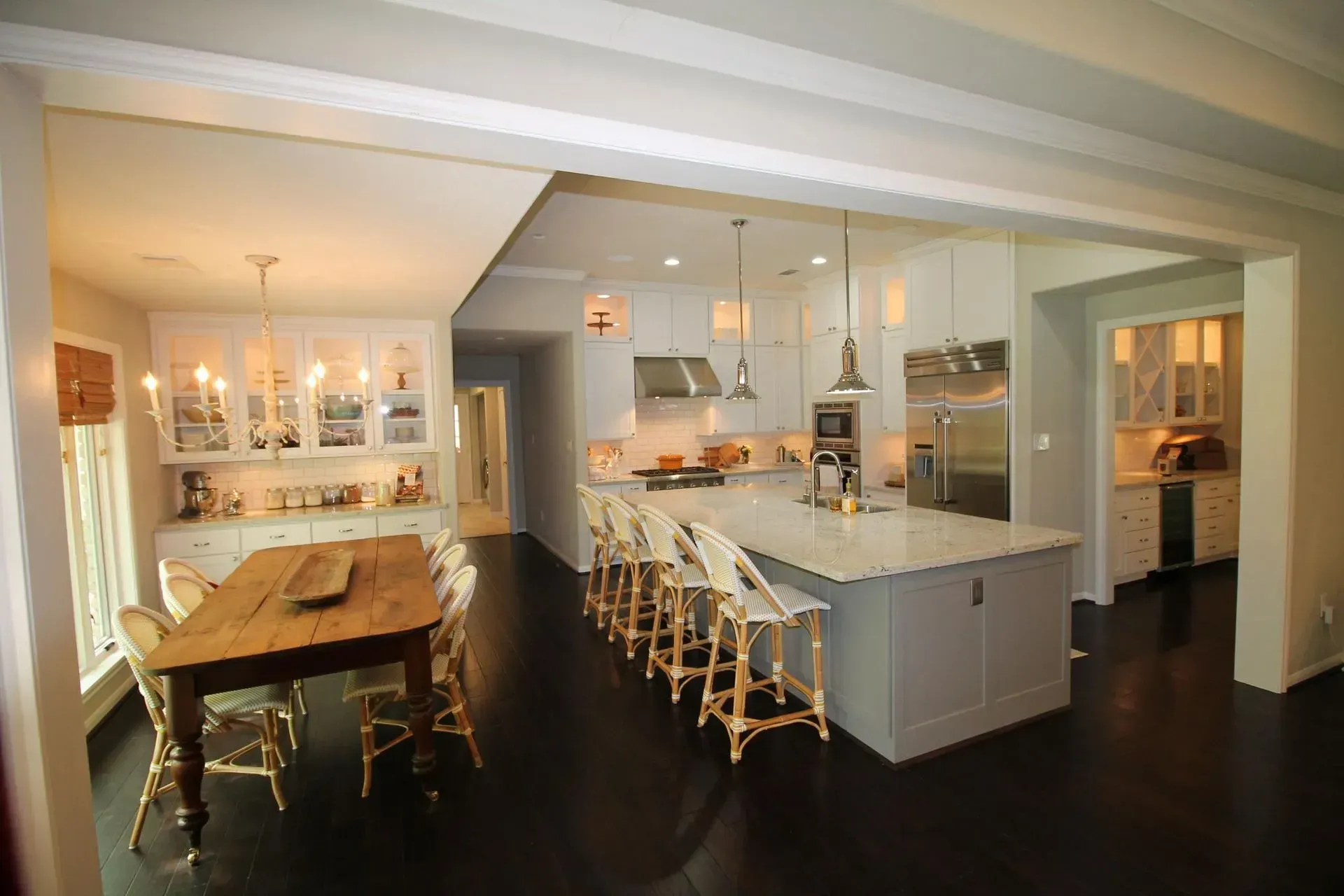 Modern open-plan kitchen and dining area with island, stools, dark floors, and a wooden dining table